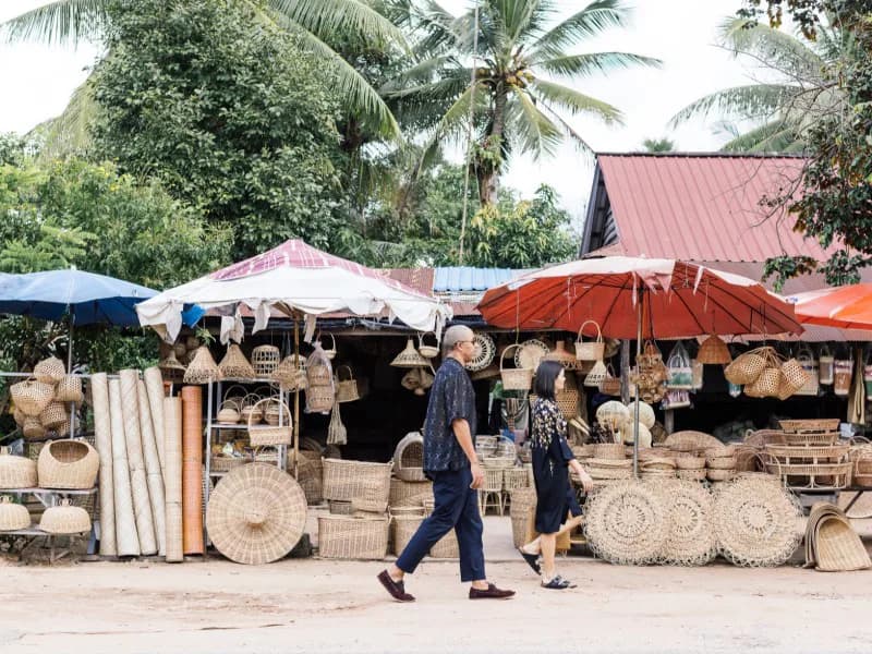 Outdoor market stall displaying woven baskets and wooden crafts under colorful umbrellas, designed by Stephen Burks Man Made.