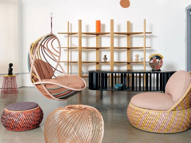 Contemporary furniture showroom with woven rattan seating, geometric wall grid installation, and black credenza display by Stephen Burks Man Made.
