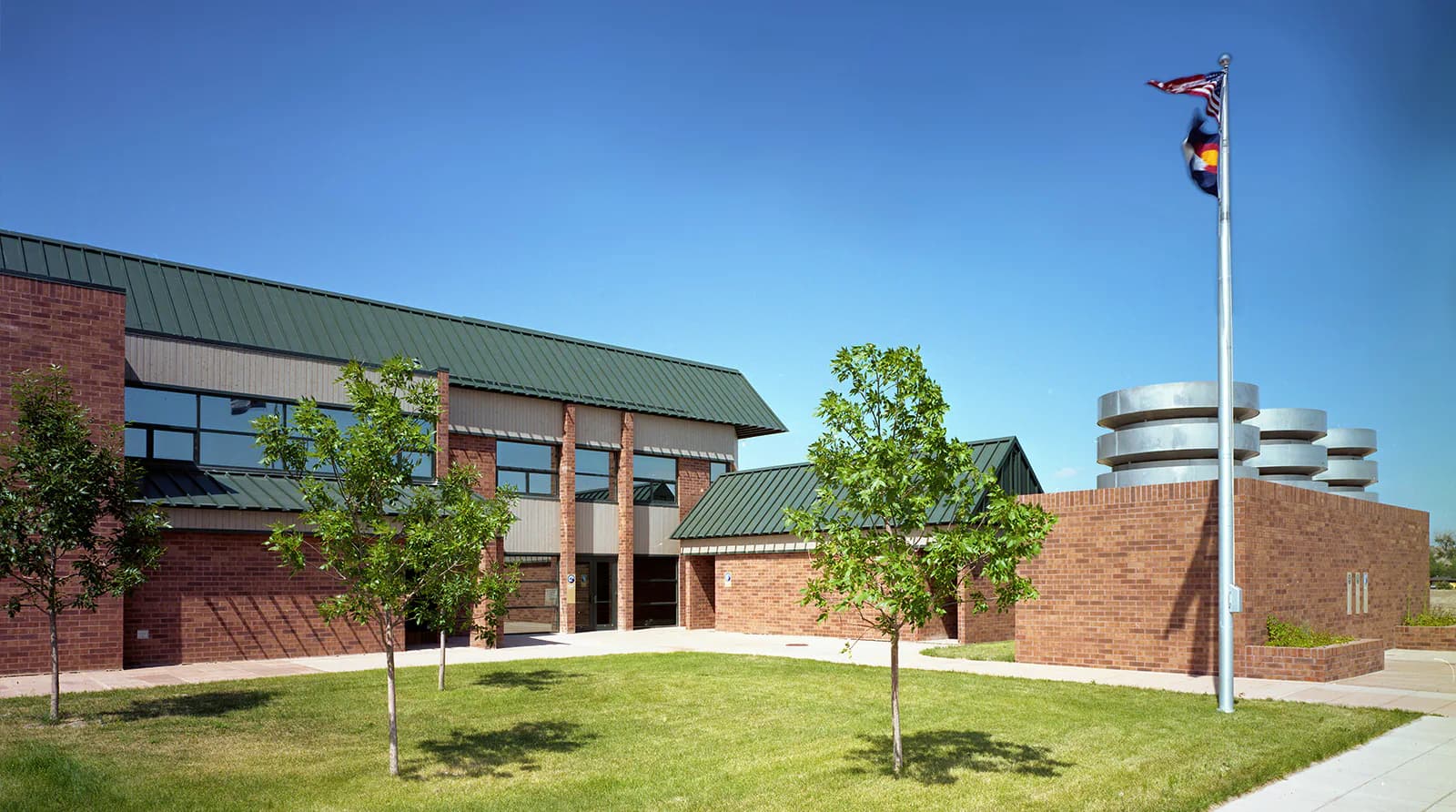 Contemporary brick institutional building with green roof, two young trees in lawn, and flagpole, designed by Stephen Ely Architect.