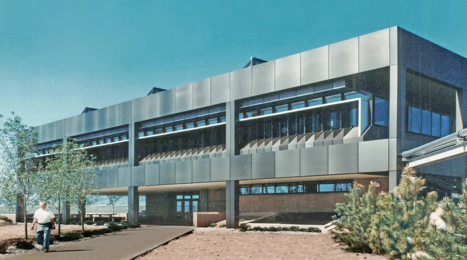 Modern institutional building with horizontal metal cladding, glass façade, and ground-level entrance, set in a desert landscape with native plantings by Stephen Ely Architect.