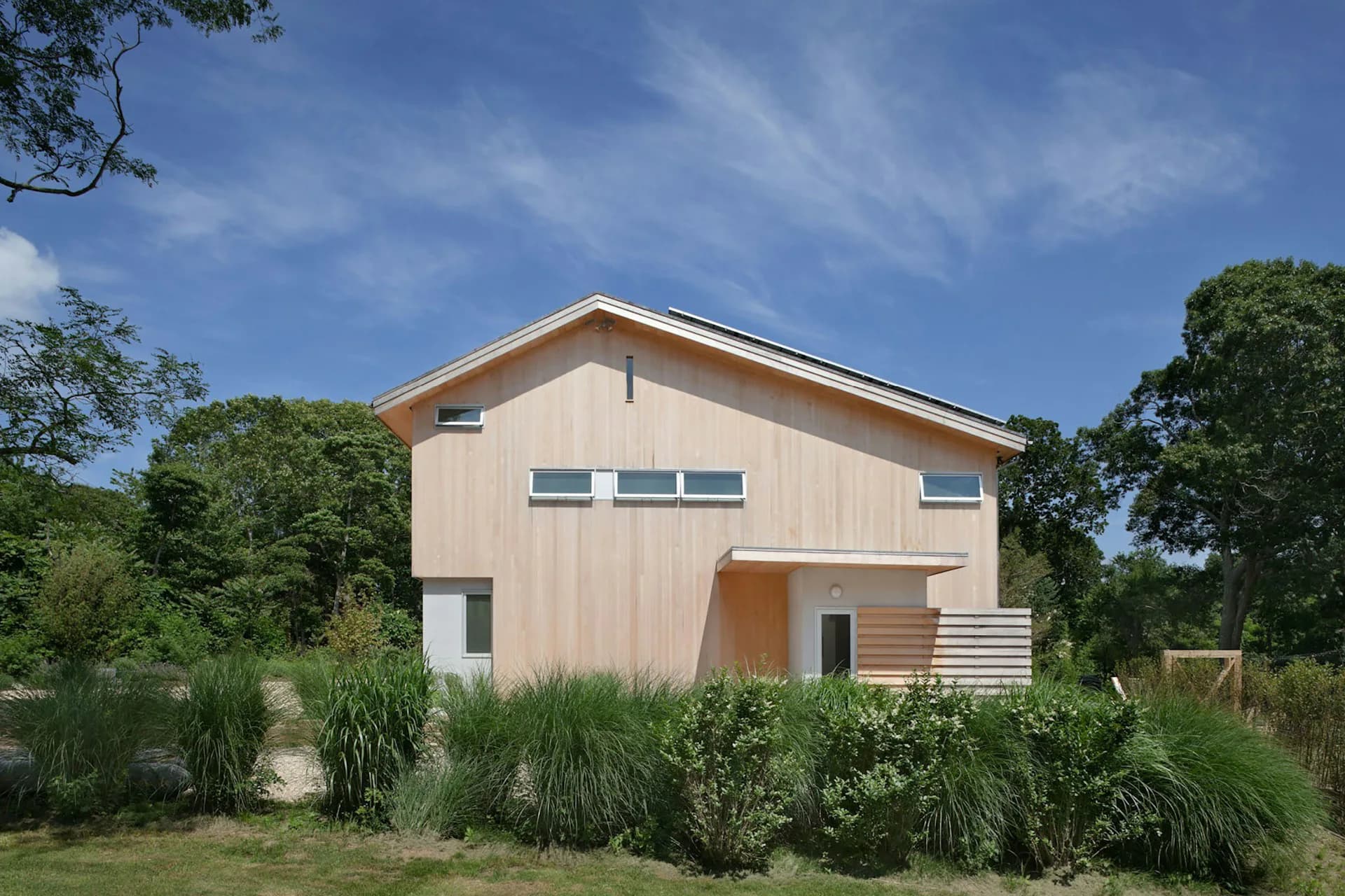 Modern residential house with warm beige exterior, large windows, and contemporary design surrounded by native landscaping by Stephen Moser Architects.