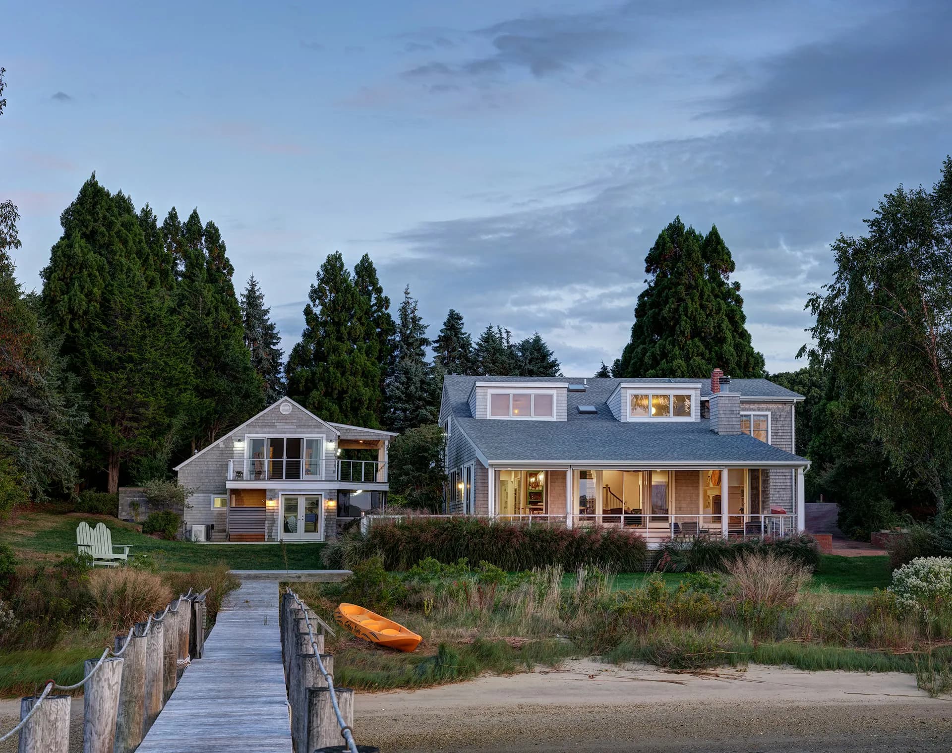 Contemporary waterfront residence with board-and-batten siding, expansive windows, and covered porch overlooking beach access by Stephen Moser Architects.