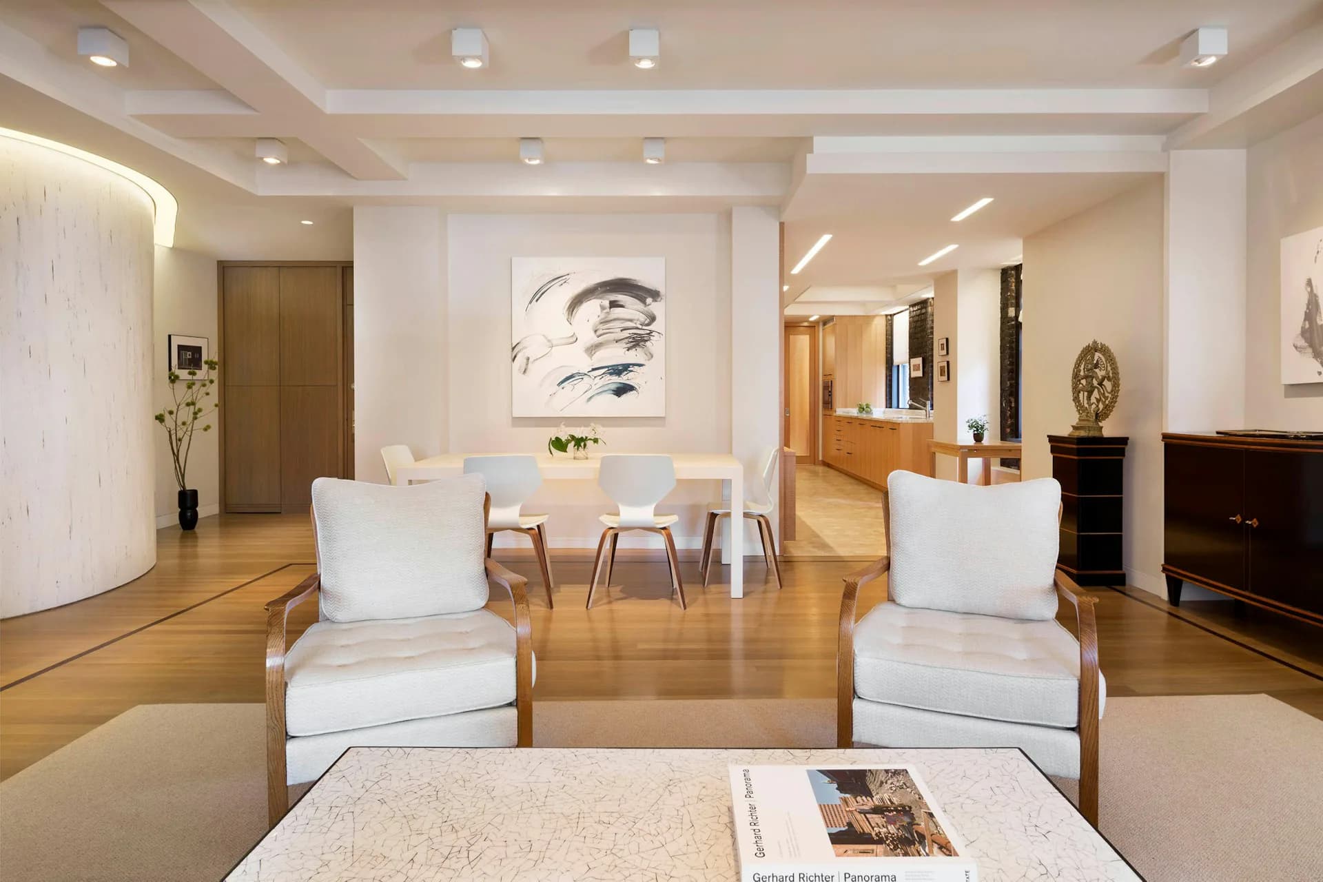 Modern residential living room with white upholstered chairs, wooden floors, coffered ceiling, and contemporary artwork by Stephen Moser Architects.
