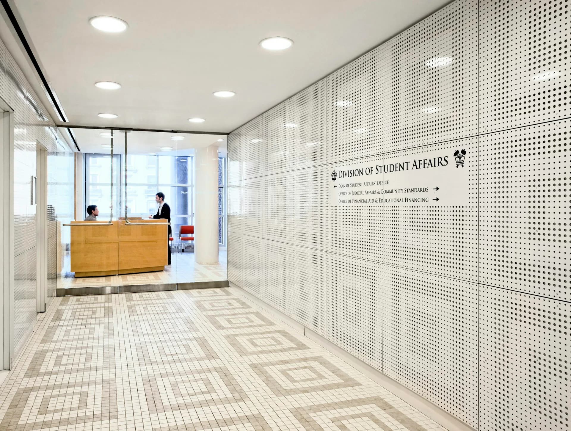 Modern office reception area with geometric patterned wall panels, wooden desk, and minimalist lighting by Stephen Yablon Architecture.