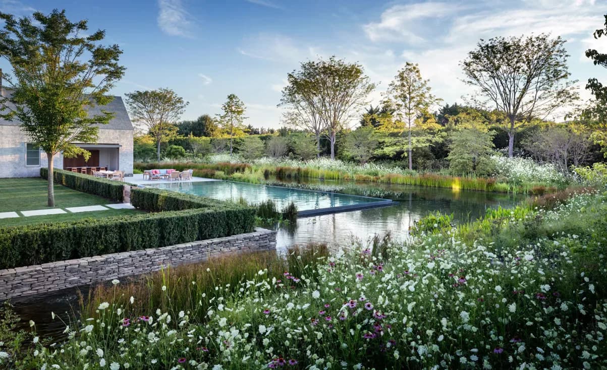 Residential landscape garden with naturalistic planting, reflecting pond, manicured hedges, and modern house visible in background by Steven Harris Architects.