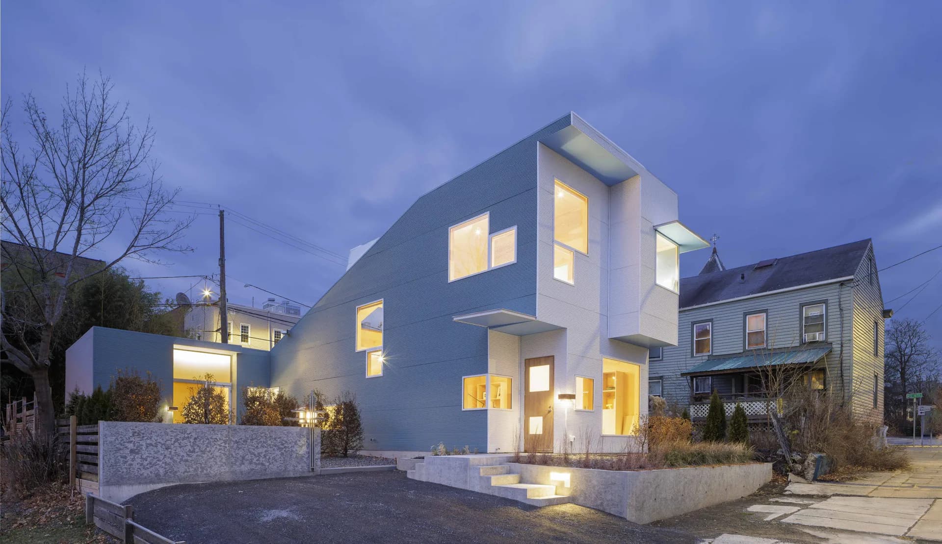 Modern white cubic residence with illuminated windows at dusk, featuring angular geometry and clean lines, by Steven Holl Architects.