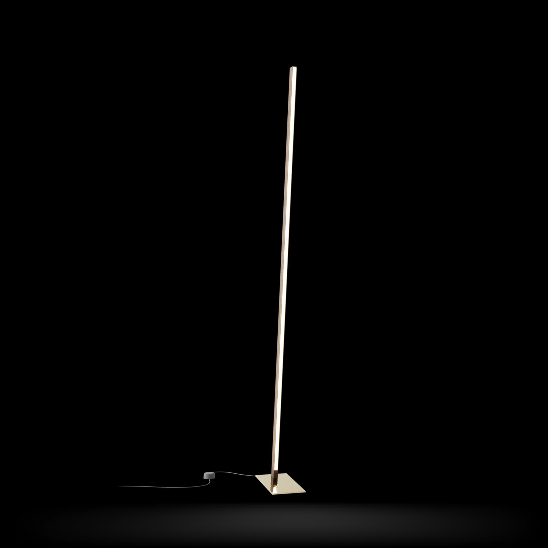 Minimalist floor lamp with slender brass stem and geometric base on white background by Stickbulb.