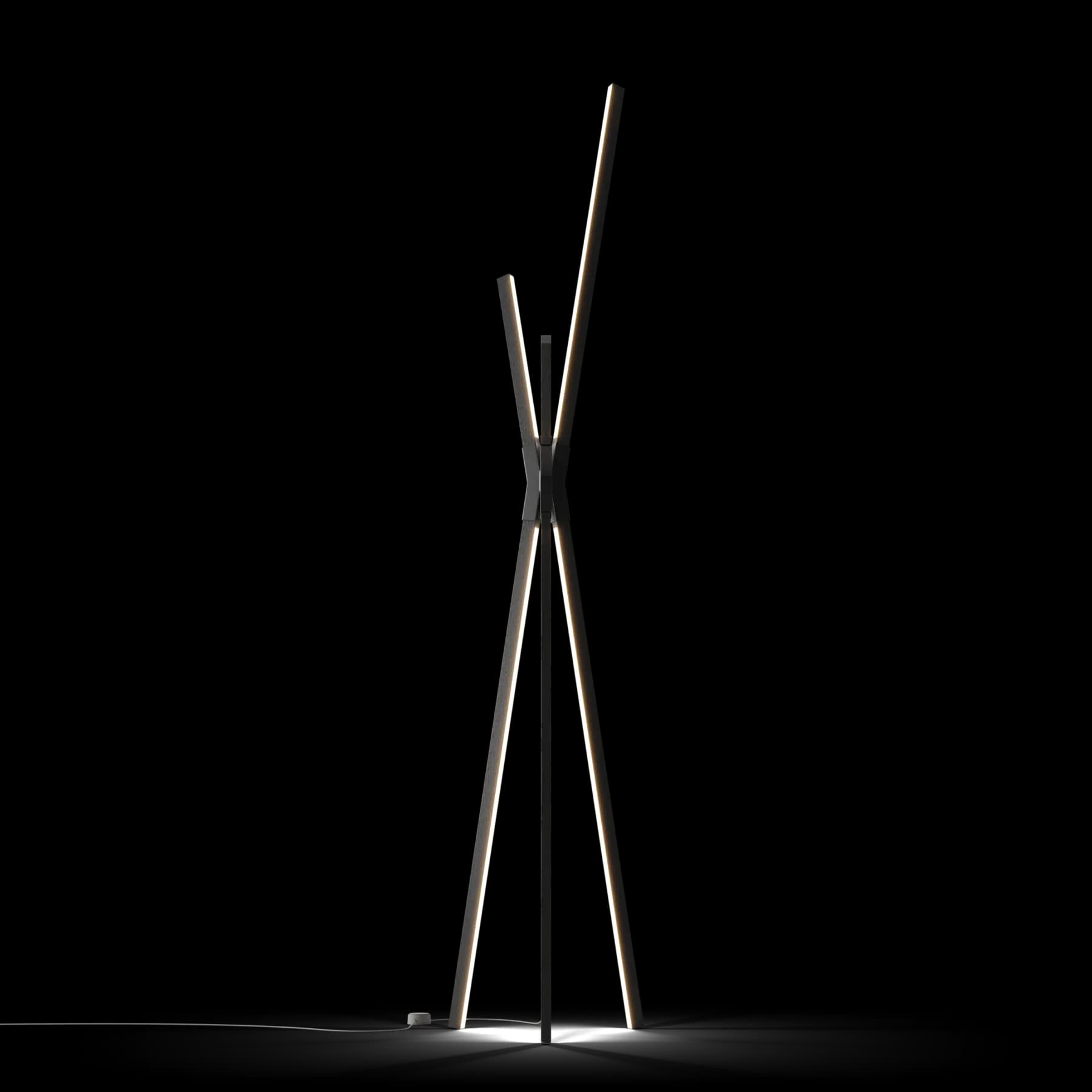 Tall, minimalist lighting installation with thin black metal rods converging at the top, creating a sculptural tripod form against a white background by Stickbulb.