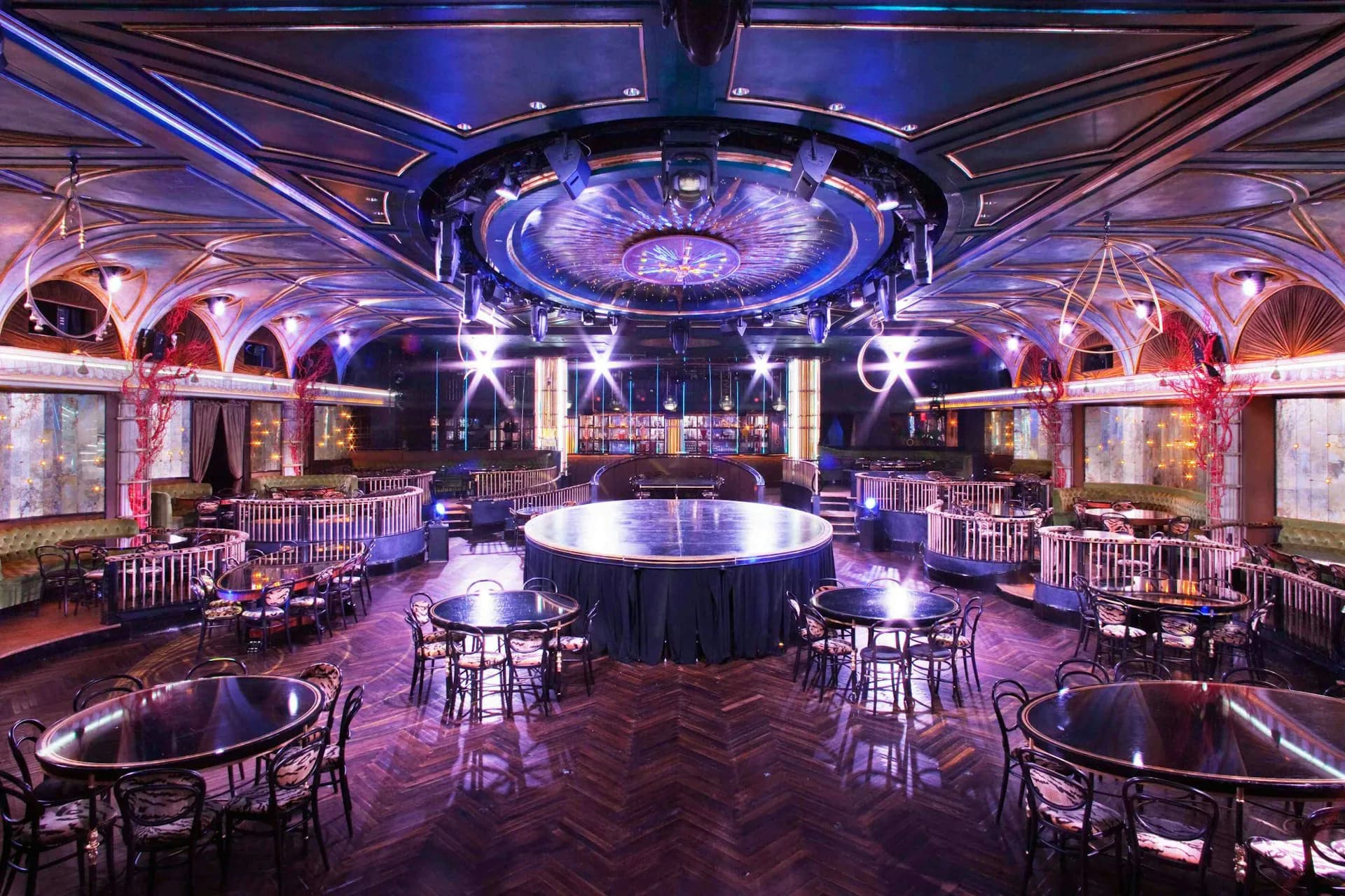 Luxurious nightclub interior with purple ambient lighting, central circular bar, symmetrical round tables, ornate arched ceilings, and dramatic illuminated dome by Stonehill Taylor.