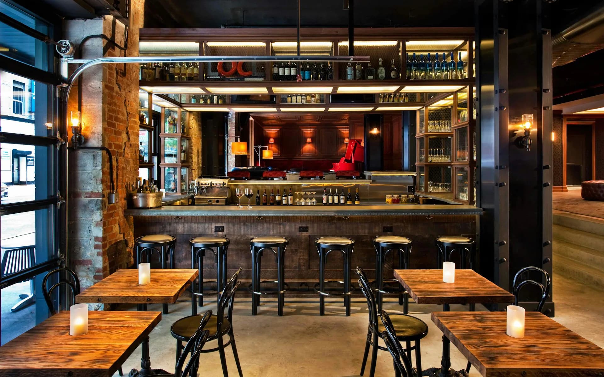 Modern bar and restaurant interior featuring wooden tables, black chairs, and a dramatic backlit bar with amber and red lighting by Stonehill Taylor.