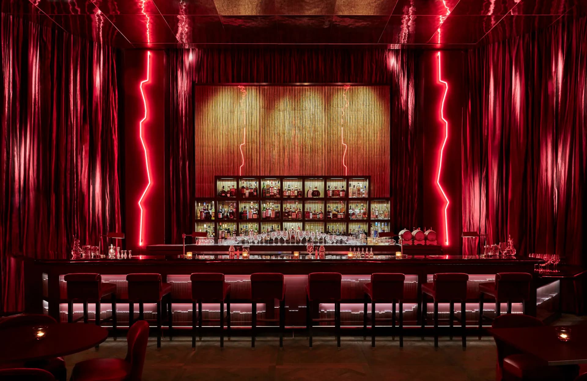 Red neon-lit theater interior with dramatic vertical lighting, curved seating, and illuminated control booth by STRATA ARCHITECTS PLLC.