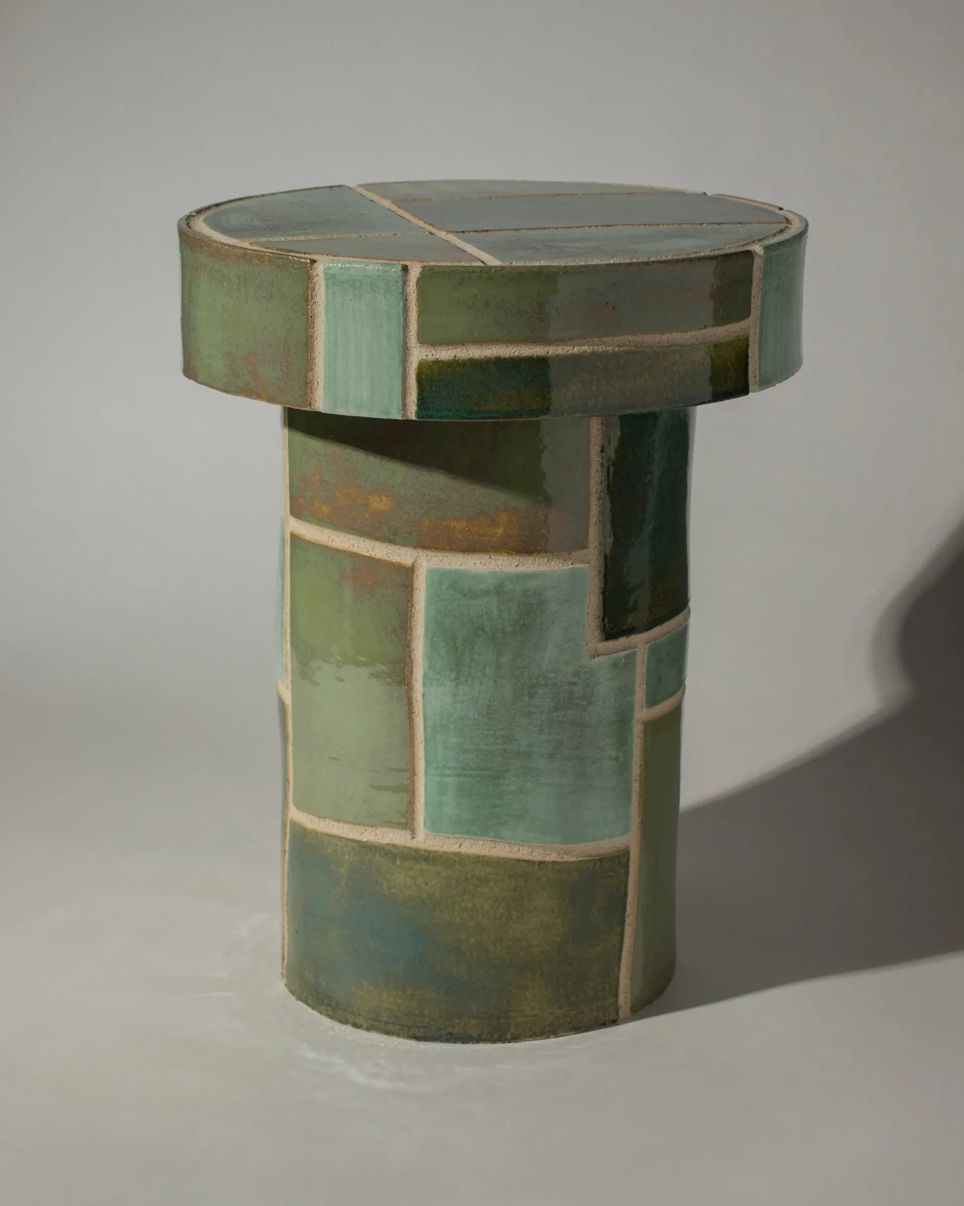 Ceramic vessel with stacked cylindrical form in patinated green and copper tones with geometric panel divisions by Streicher Goods.