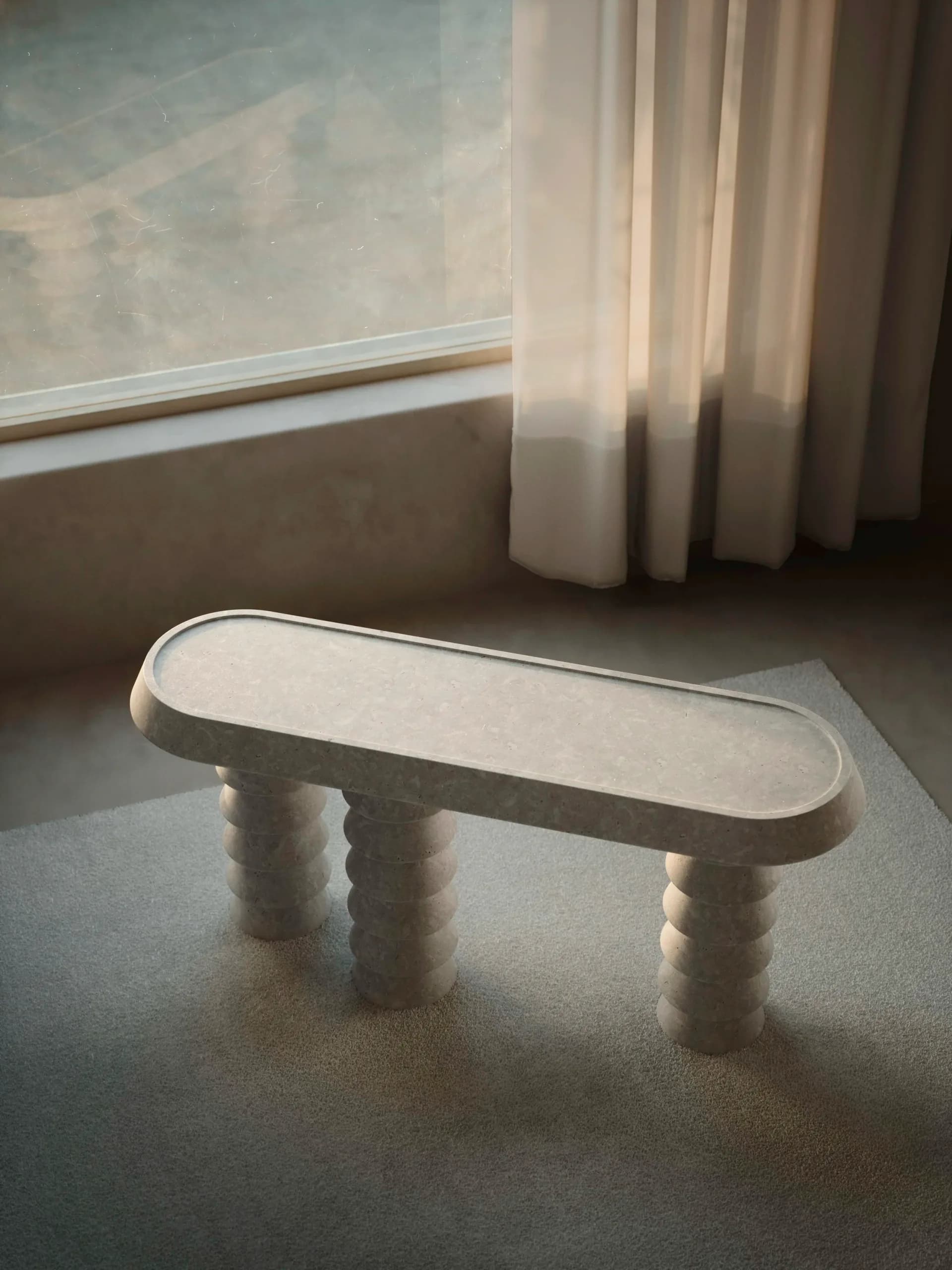 Minimalist white sculptural bench with rounded rectangular seat and cylindrical legs displayed in bright studio space by Studio Anansi.