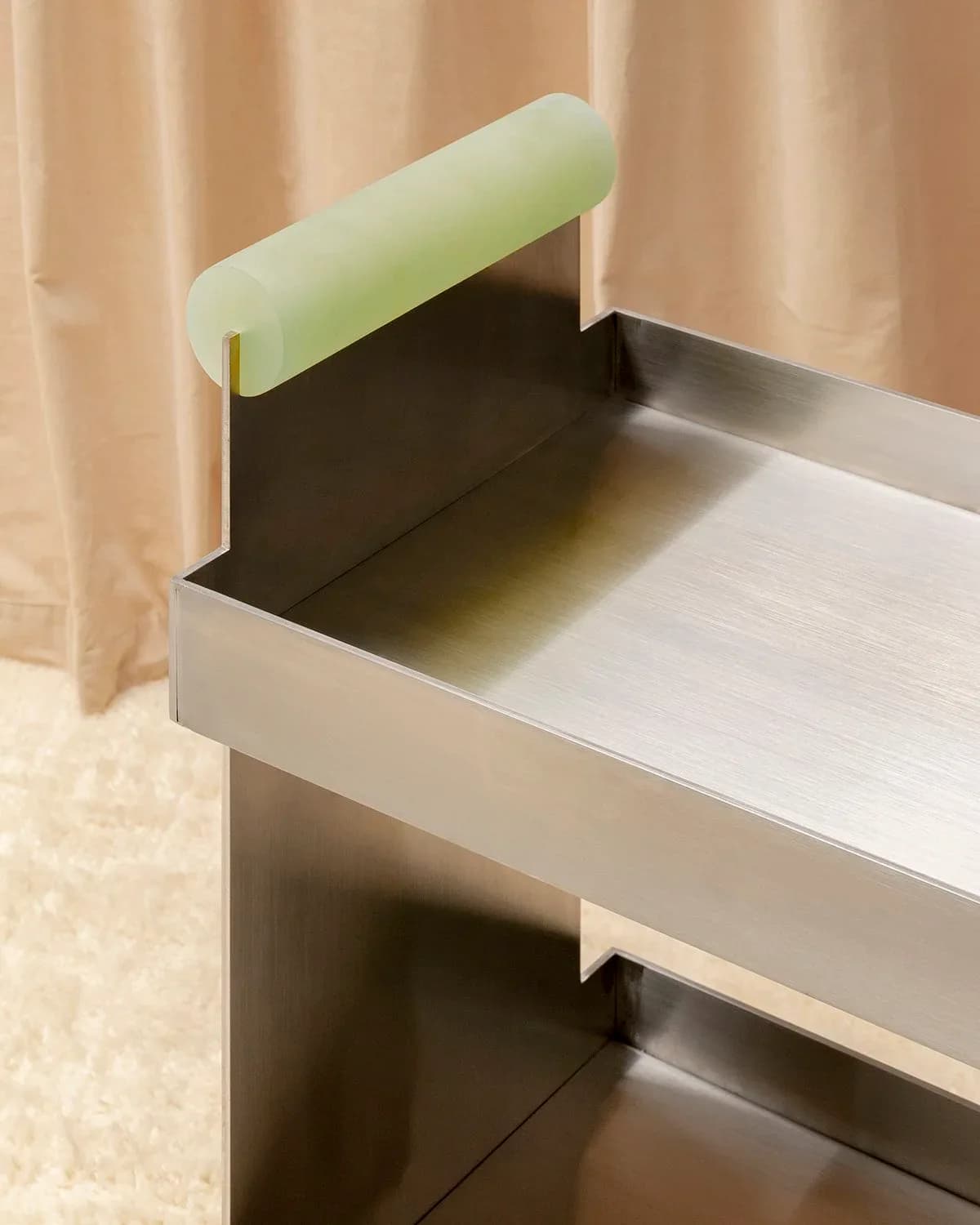 Minimalist furniture detail with pale green cylindrical element and dark metal frame on light surfaces by Studio Anansi.