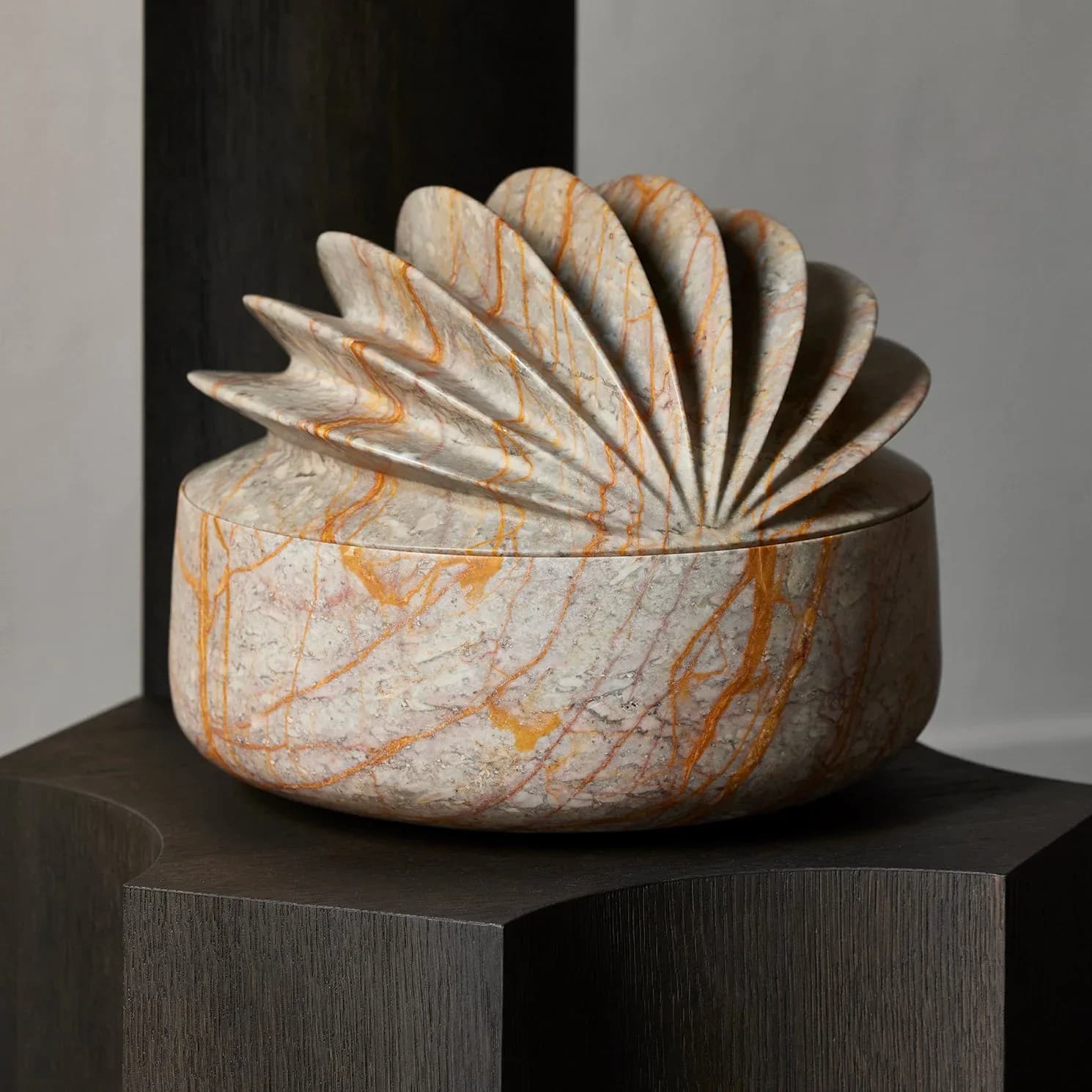 Sculptural ceramic vessel with cream and orange patterned bowl base topped with fanned leaf-like forms, displayed on dark wood pedestal by Studio Anansi.