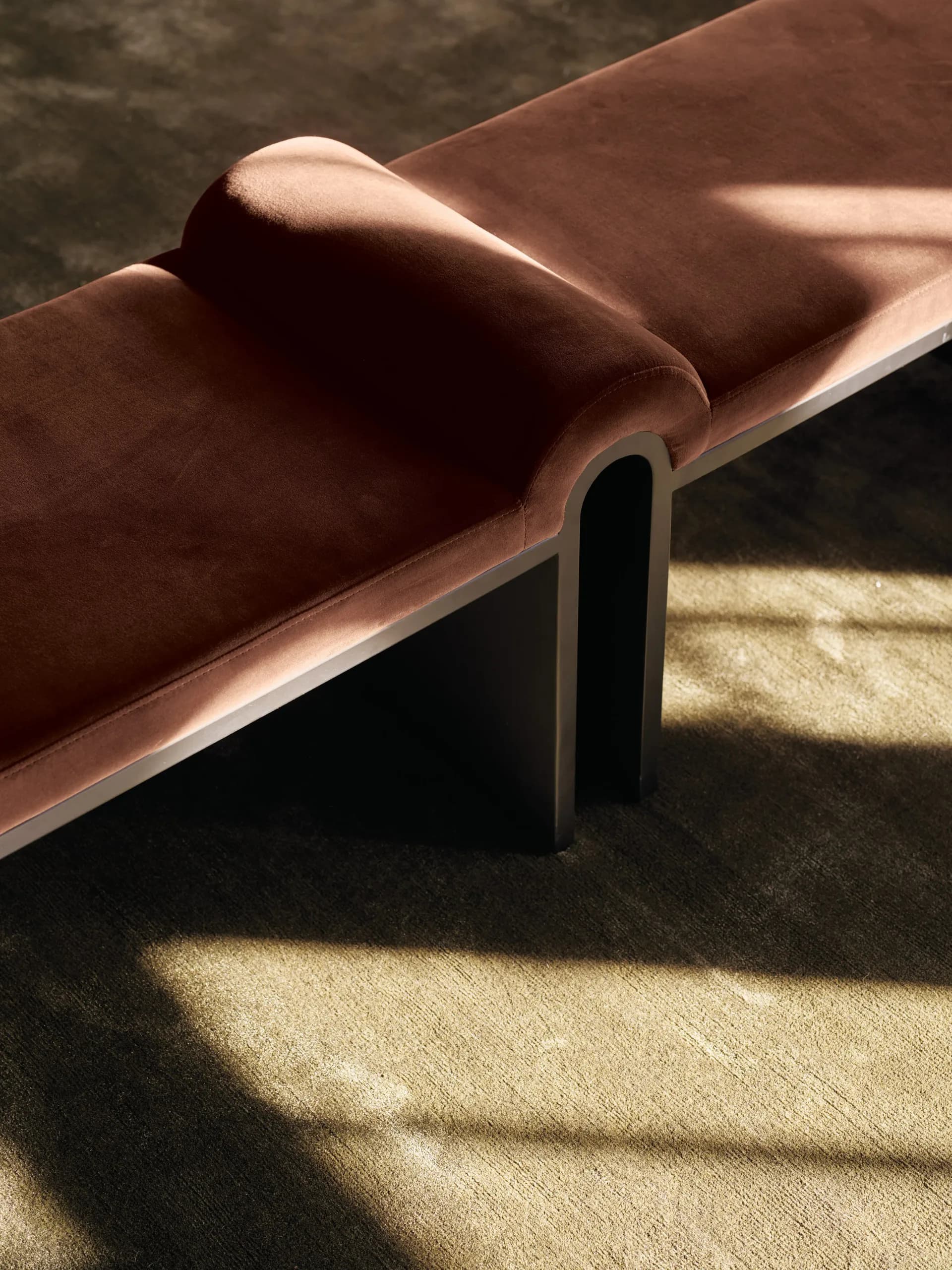 Minimalist leather chaise lounge with rolled armrest and metal legs on concrete floor, bathed in natural light, by Studio Anansi.