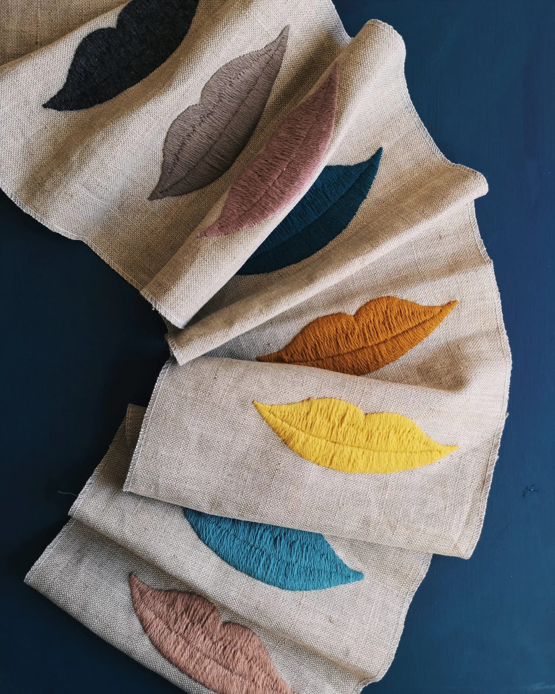 Embroidered leaf motifs in varied colors—black, gray, mauve, orange, yellow, blue, and rose—on natural linen samples by Studio Four NYC.