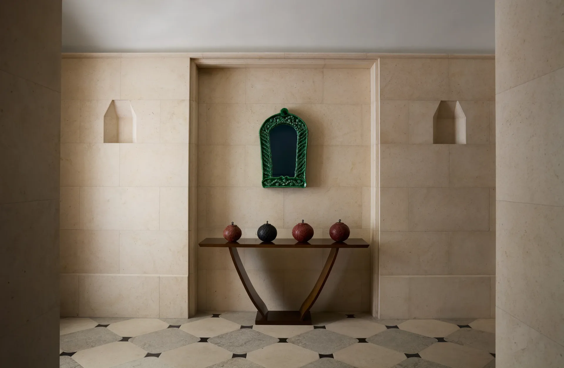 Minimalist interior with arched niche containing green mirror, console table with spherical objects, and geometric floor pattern by Studio Valle de Valle.