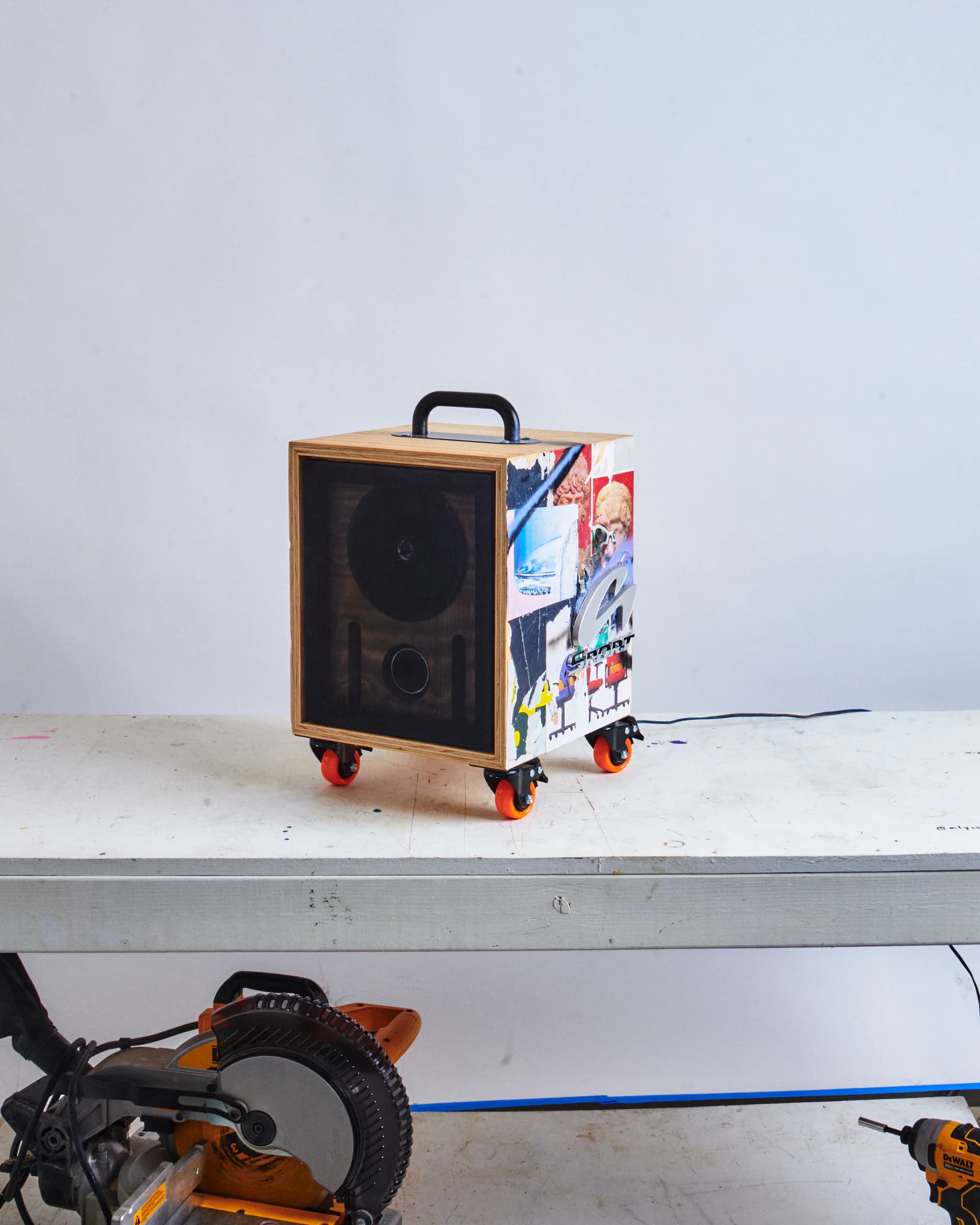 Custom portable speaker installation with wooden frame, speaker cones, and colorful graphic vinyl wrapping, featuring orange wheels and black handle by Studio Guapo.