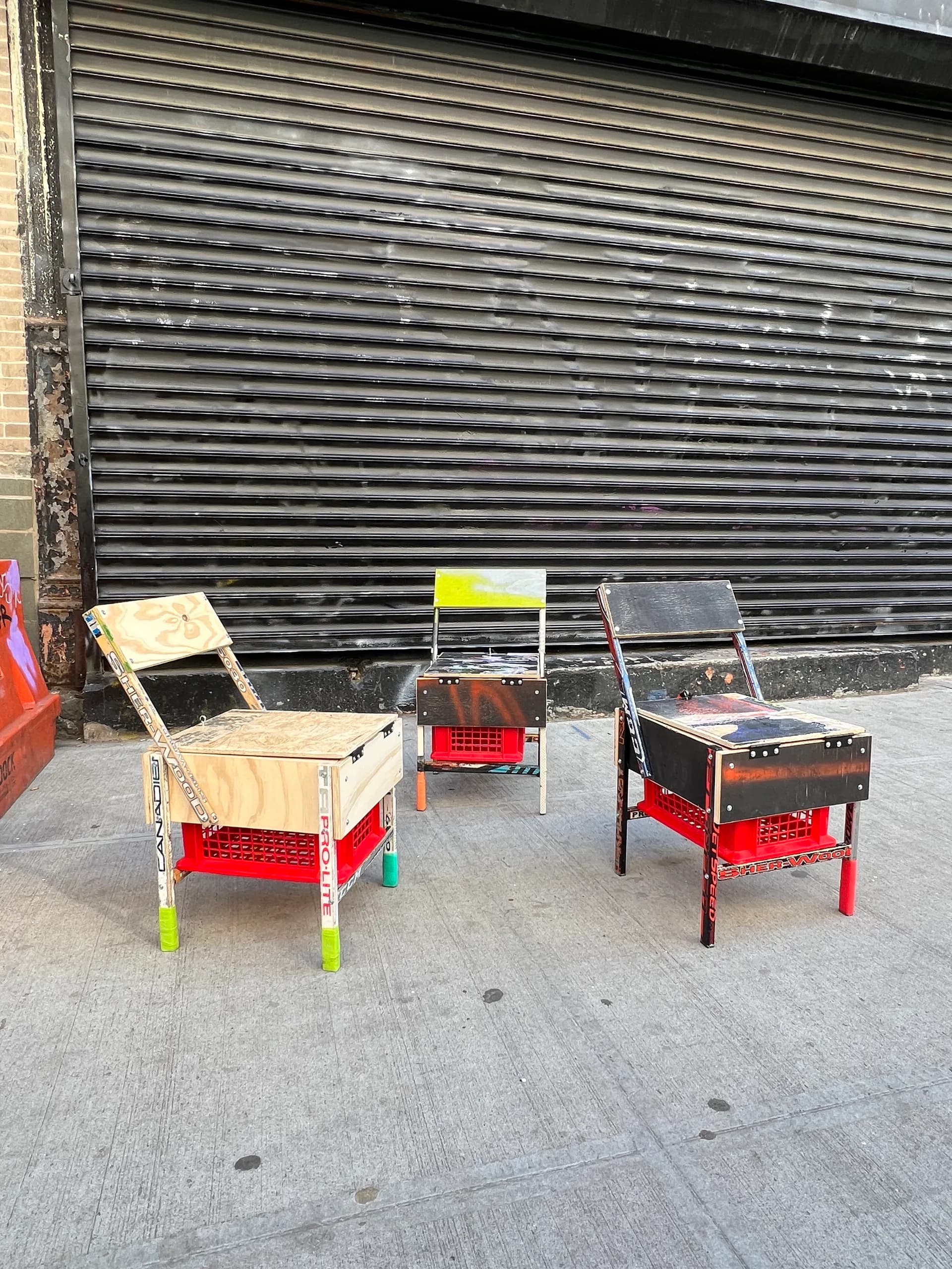 Three custom wooden and metal chairs with red crate bases and neon yellow accents arranged against a dark corrugated metal shutter by Studio Guapo.
