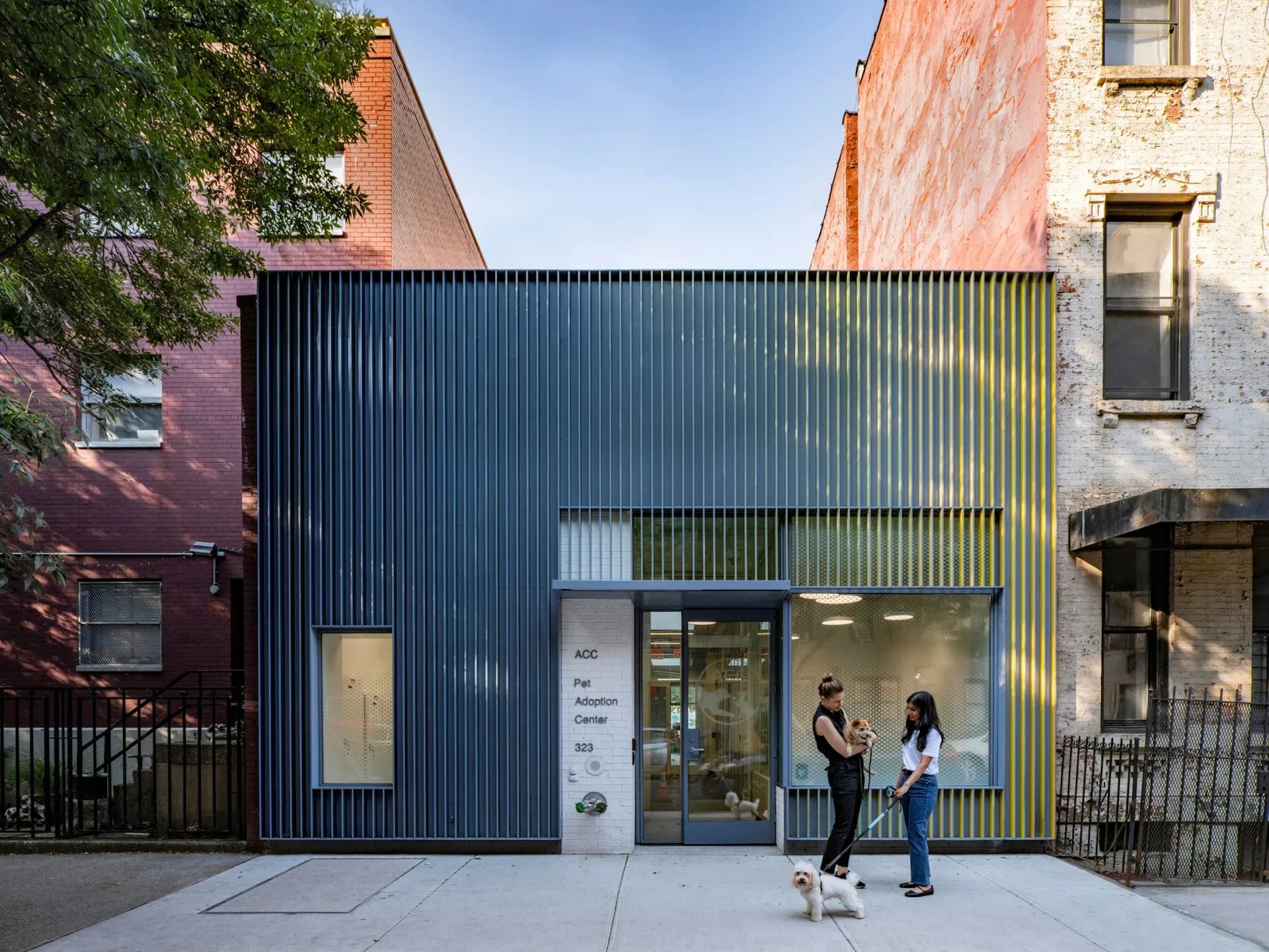 Modern storefront with dark corrugated metal facade and large glazed entry, nestled between historic brick buildings, designed by Studio Joseph.