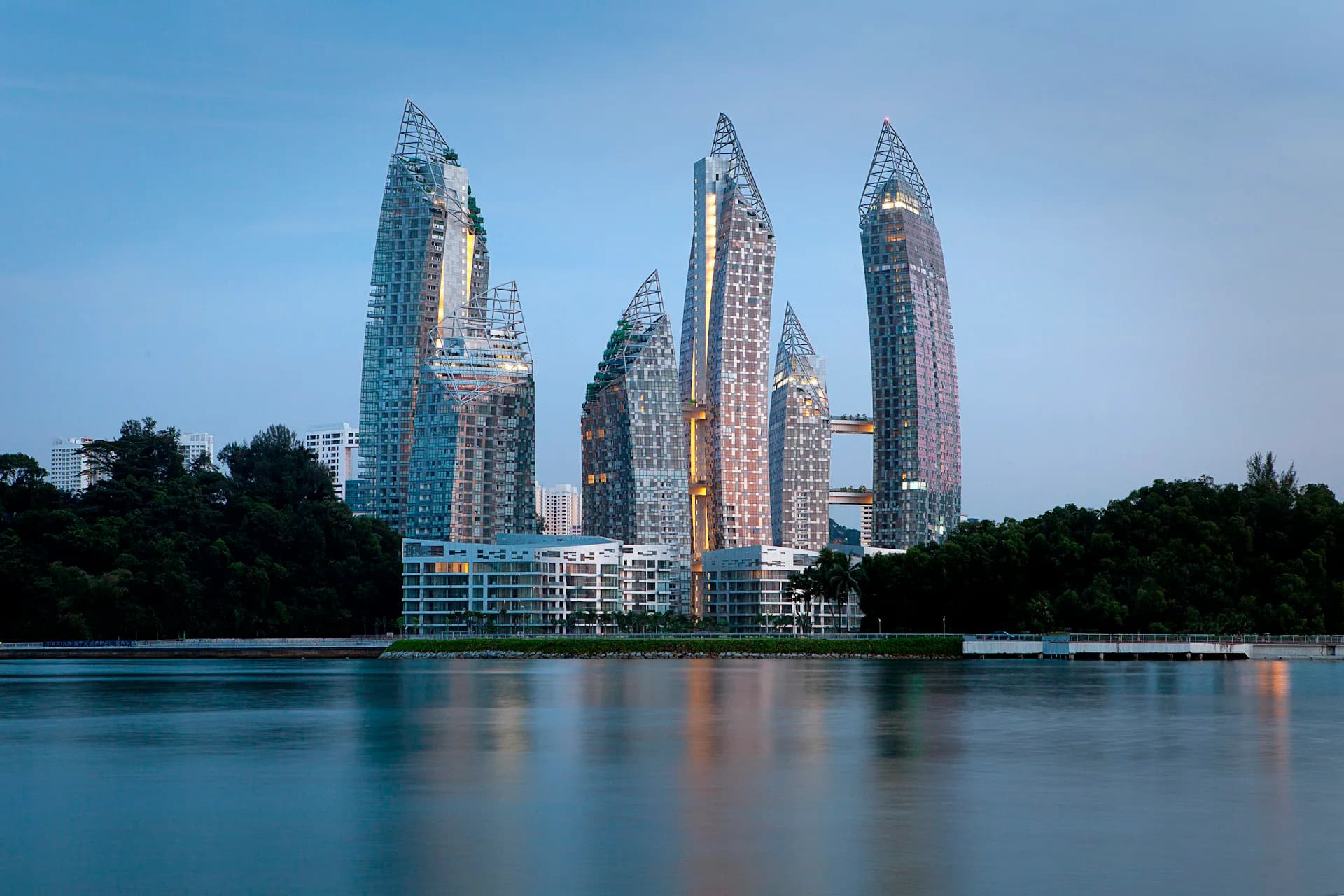 Cluster of crystalline residential towers with distinctive angular glass facades reflected in calm water at dusk, by Studio Libeskind.