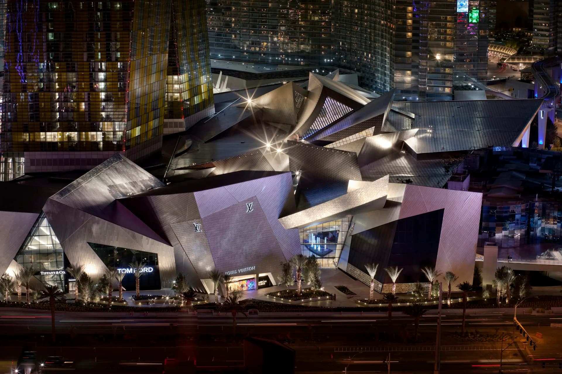 Illuminated metallic sculptural building with angular faceted surfaces rises against nighttime cityscape, designed by Studio Libeskind.
