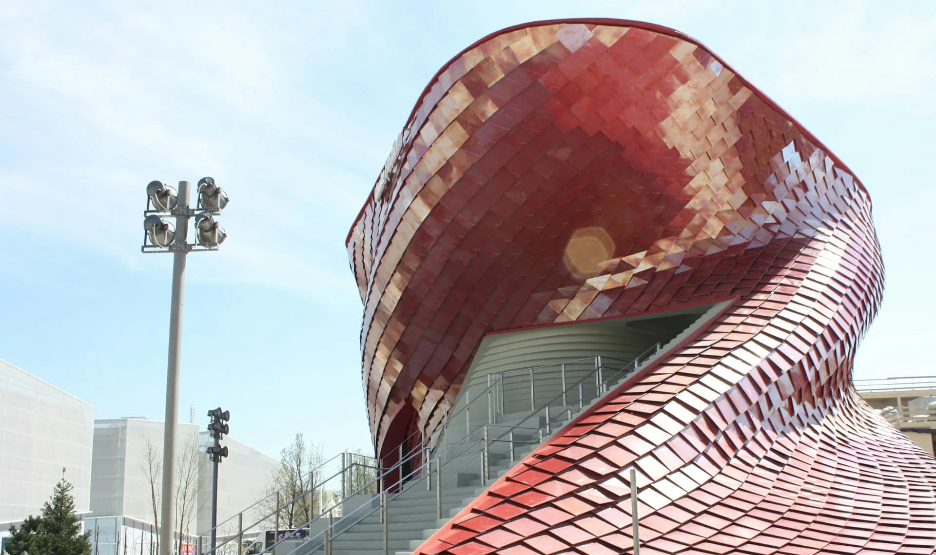 Red-tiled curved architectural facade with dramatic swooping forms and geometric patterning, a contemporary building design by Studio Libeskind.