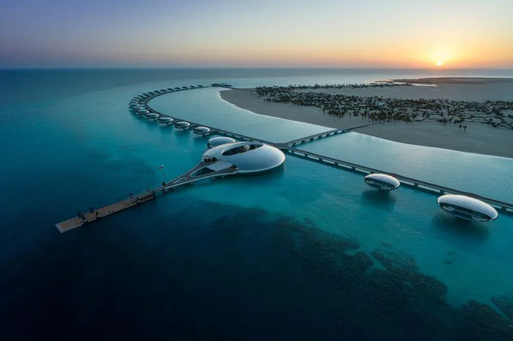 Futuristic coastal development with curved white architecture and serpentine causeways set in turquoise waters at sunset, by Studio Paolo Ferrari.