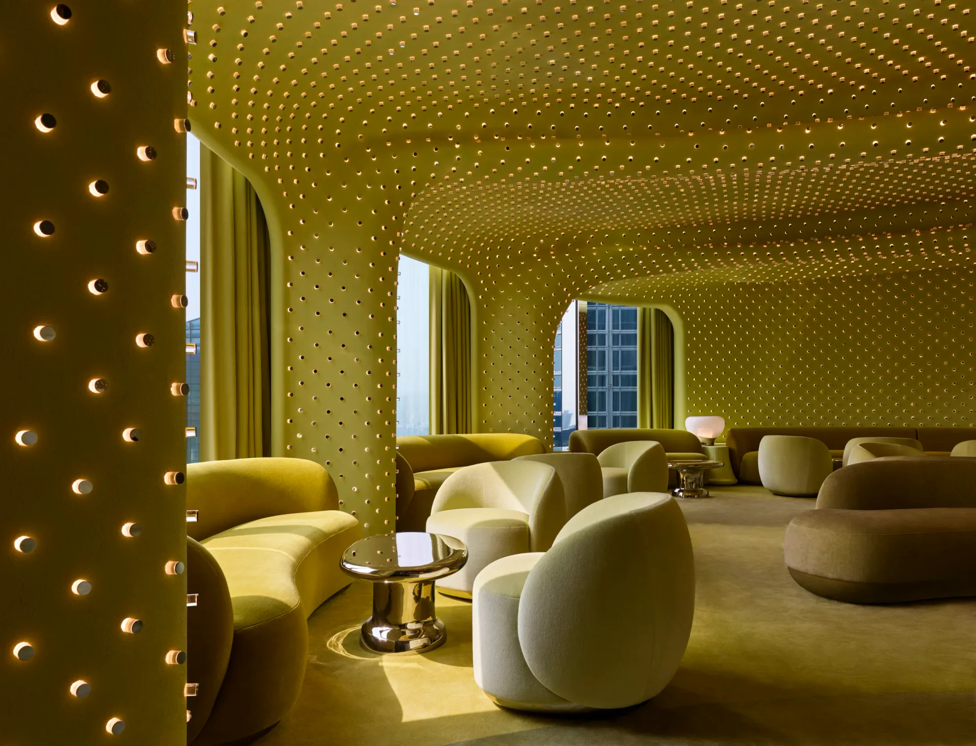 Golden luxury lounge with perforated walls, curved seating, ambient lighting, and floor-to-ceiling windows by Studio Paolo Ferrari.