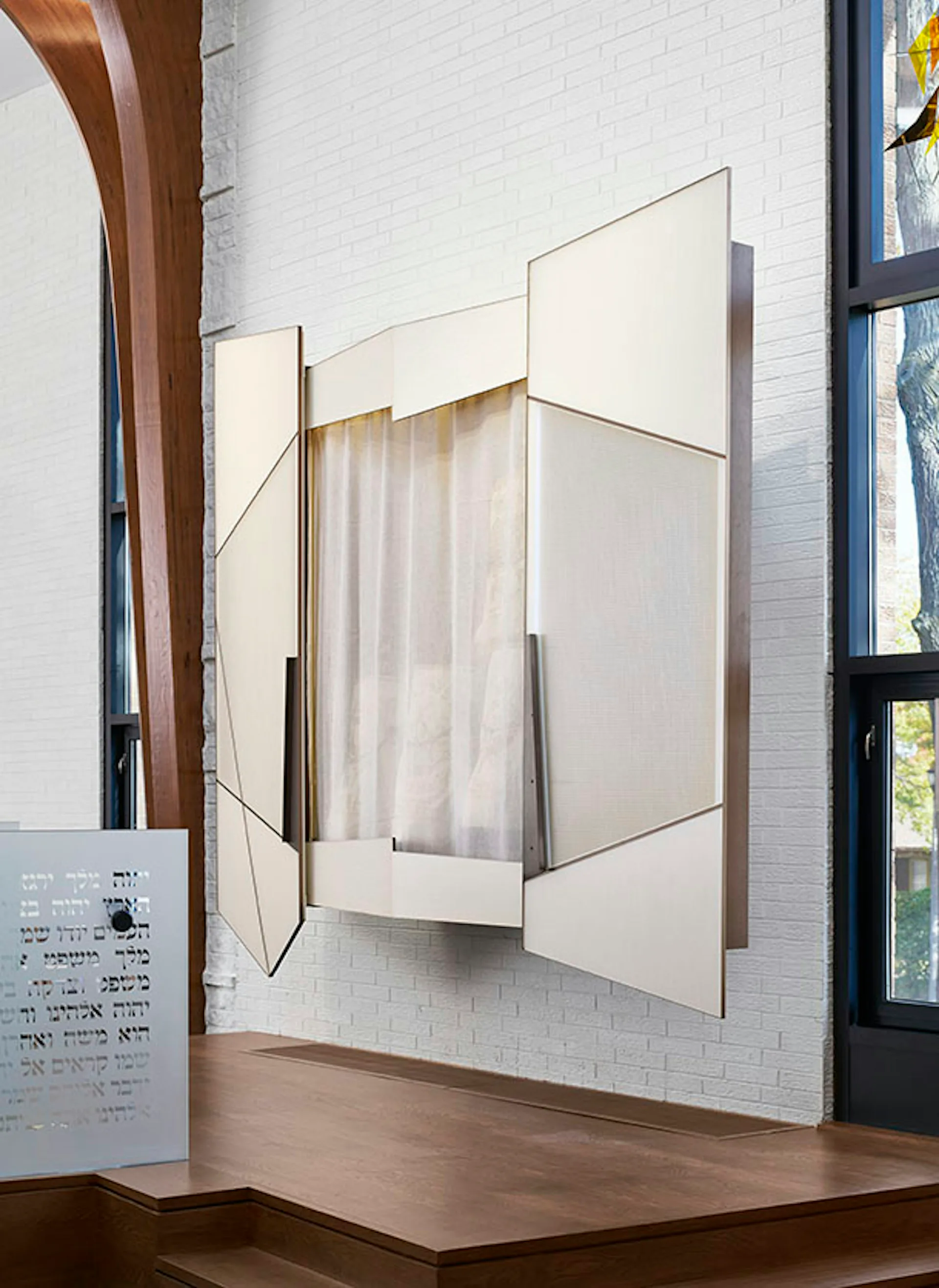 Modern white brick gallery space featuring an angular sculptural installation with cream fabric draping and metal framing elements by Studio ST Architects.