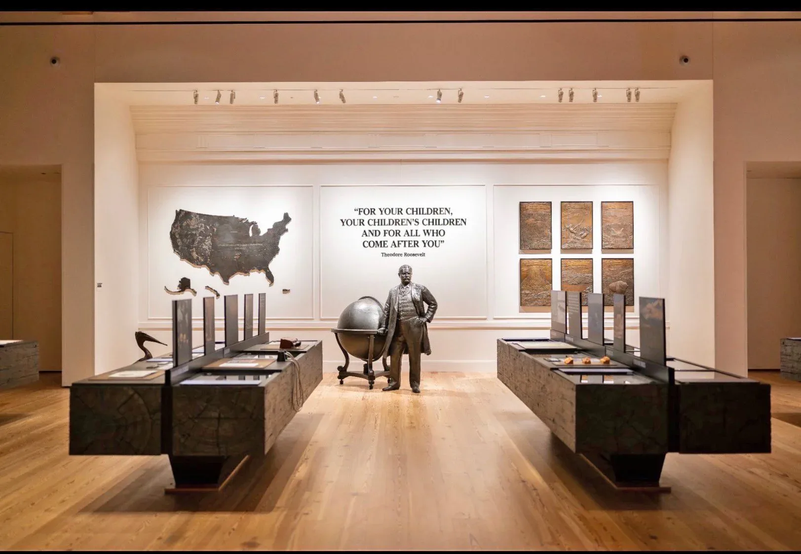Museum exhibition gallery with wooden flooring, white walls, and black display pedestals featuring a US map, globe, and framed artwork by StudioEIS.