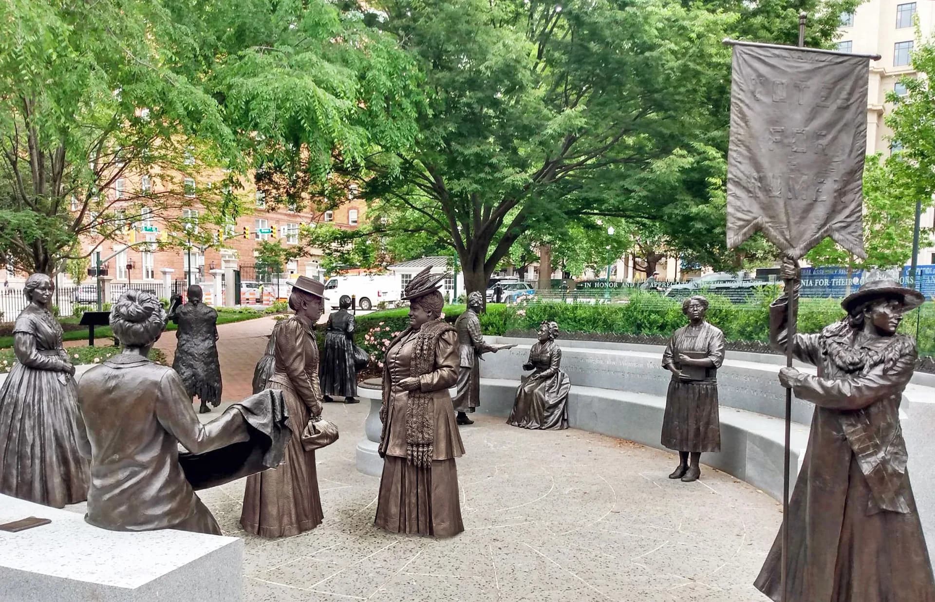 Bronze sculptural figures arranged in an urban plaza with trees and historic buildings, a public art installation by StudioEIS.