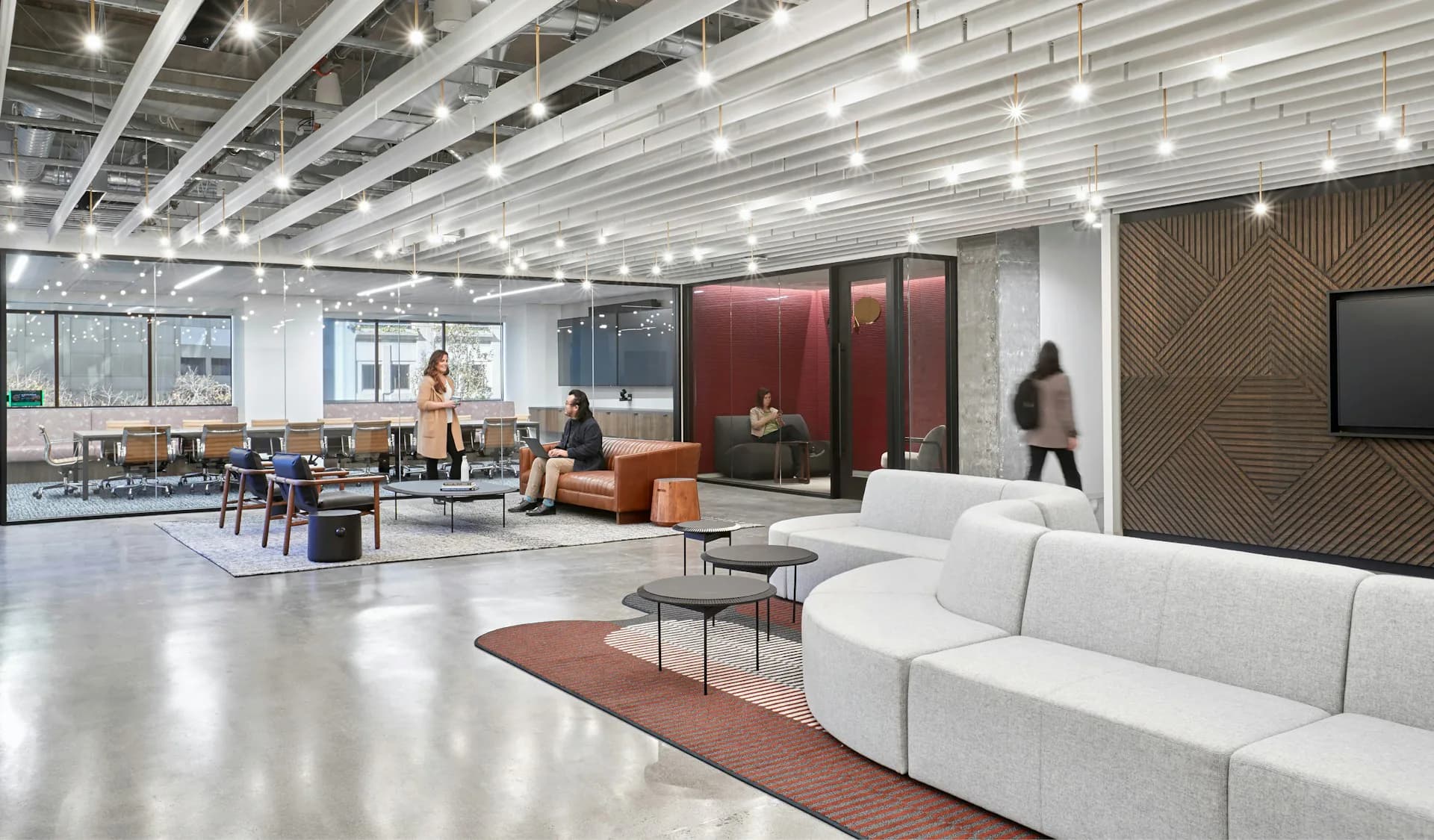 Modern office lounge with white sectional sofa, warm wood accents, polished concrete floors, and industrial ceiling by STUDIOS Architecture.