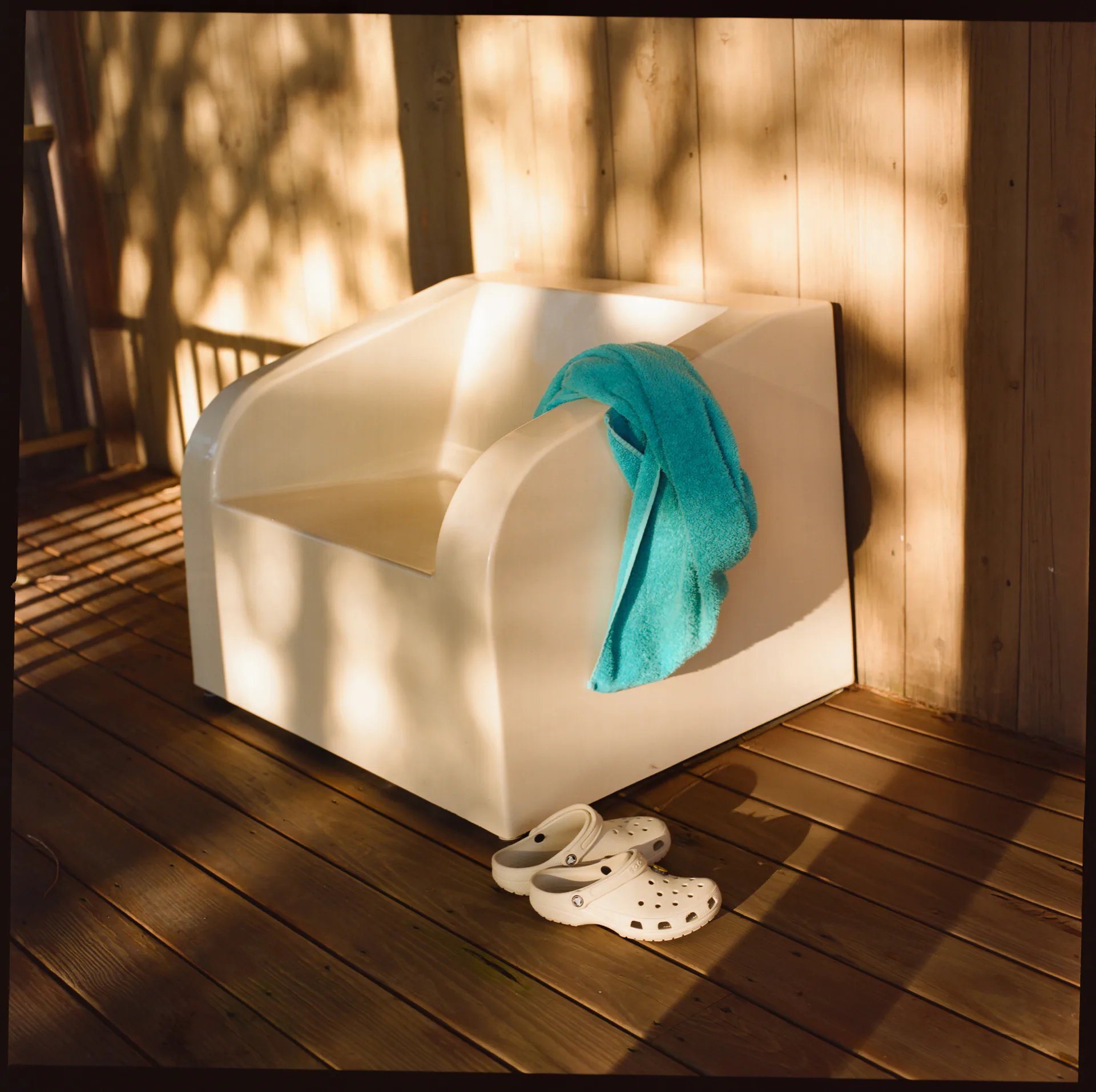 White sculptural cube installation with turquoise fabric element on wooden deck, casting dramatic shadows in natural sunlight by Sun Set.