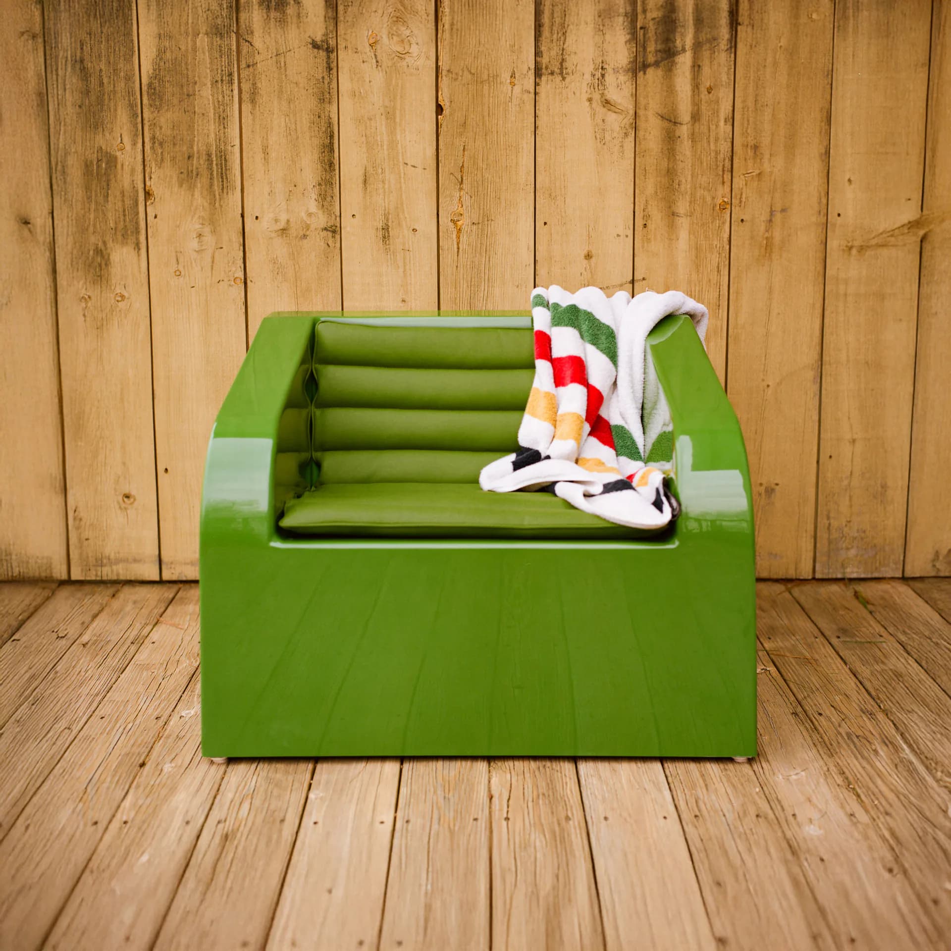 Bright green storage box with rolled green fabric and colorful striped textiles on wooden floor backdrop by Sun Set.