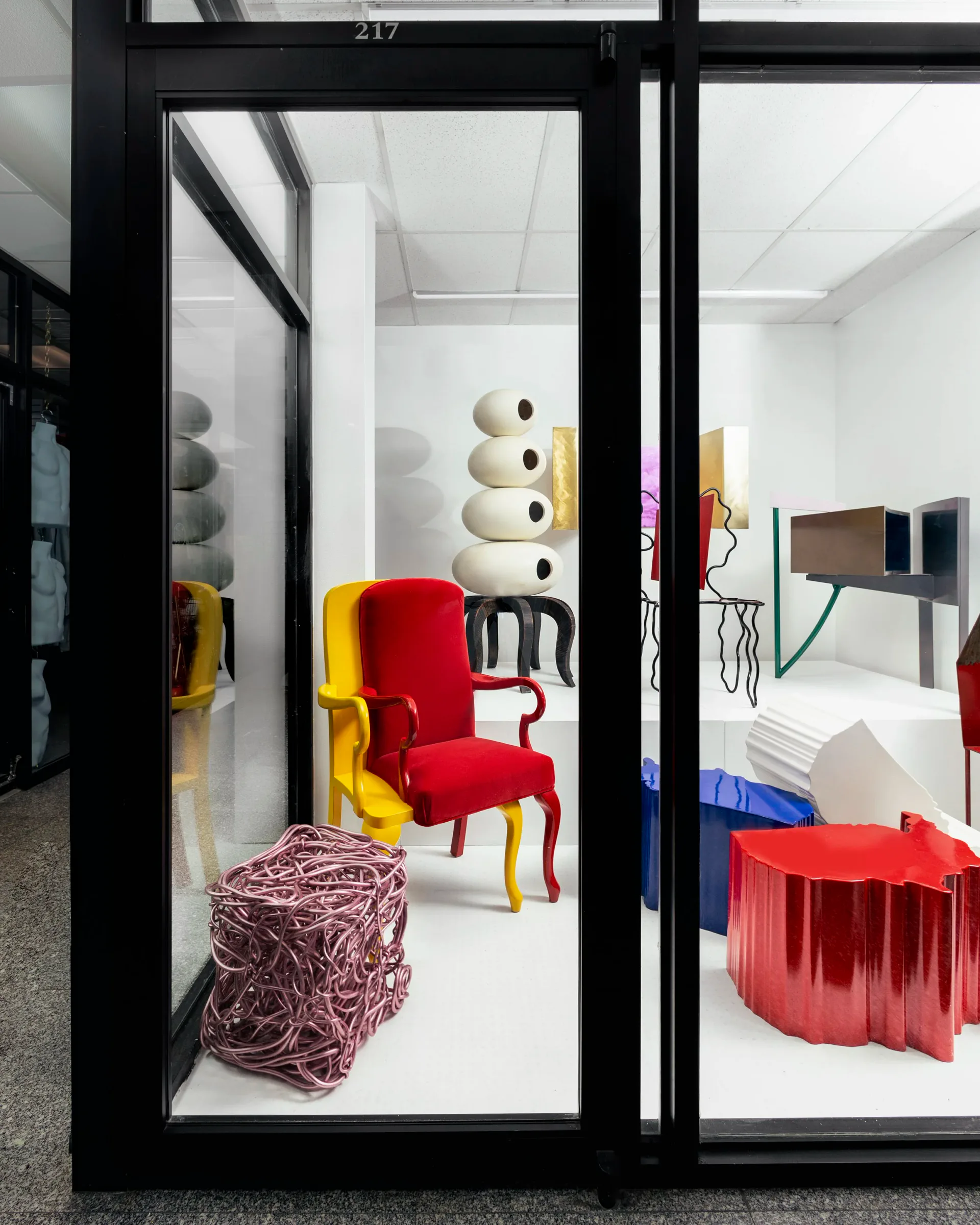 Interior design installation featuring a red velvet chair with gilt legs, cream sculptural vessels, and red fabric elements in a minimalist white gallery space by Superhouse.