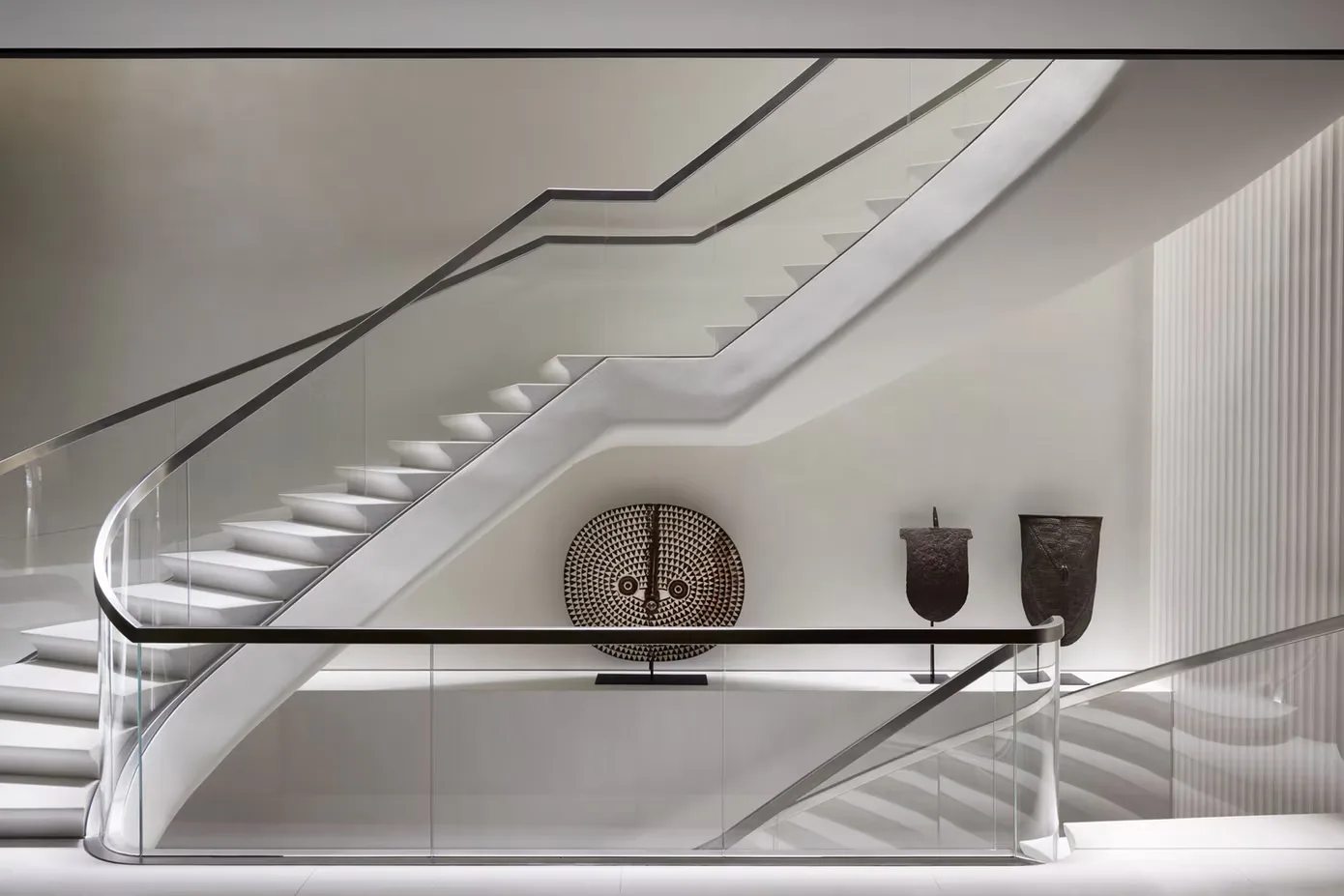 Minimalist staircase with curved white walls and metal railings, displaying sculptural vessels on a floating shelf by SuperStrata.