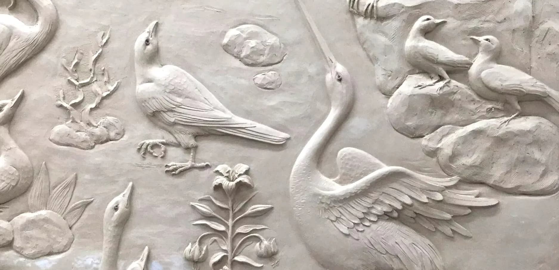 Ornamental plaster relief wall featuring classical botanical and avian motifs in white, including swans, flowers, and decorative foliage by SuperStrata.