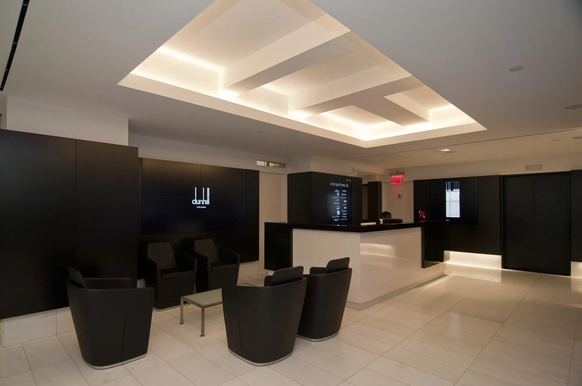Modern lobby featuring curved black seating, polished white flooring, geometric coffered ceiling with integrated lighting, and dark accent walls by Sydness Architects.