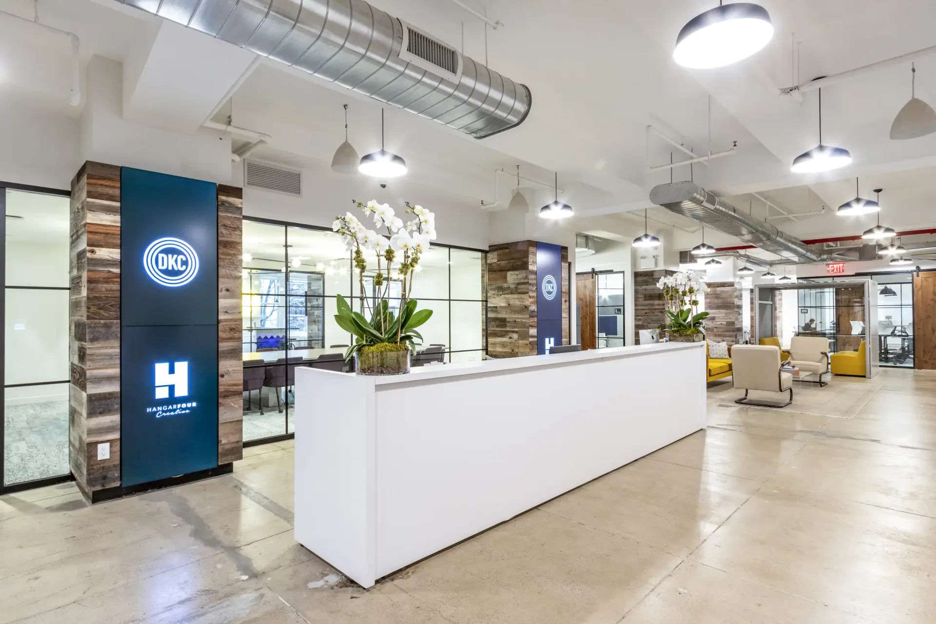 Modern office reception area with white desk, blue branding panels, industrial ceiling, and polished concrete floors by Sydness Architects.
