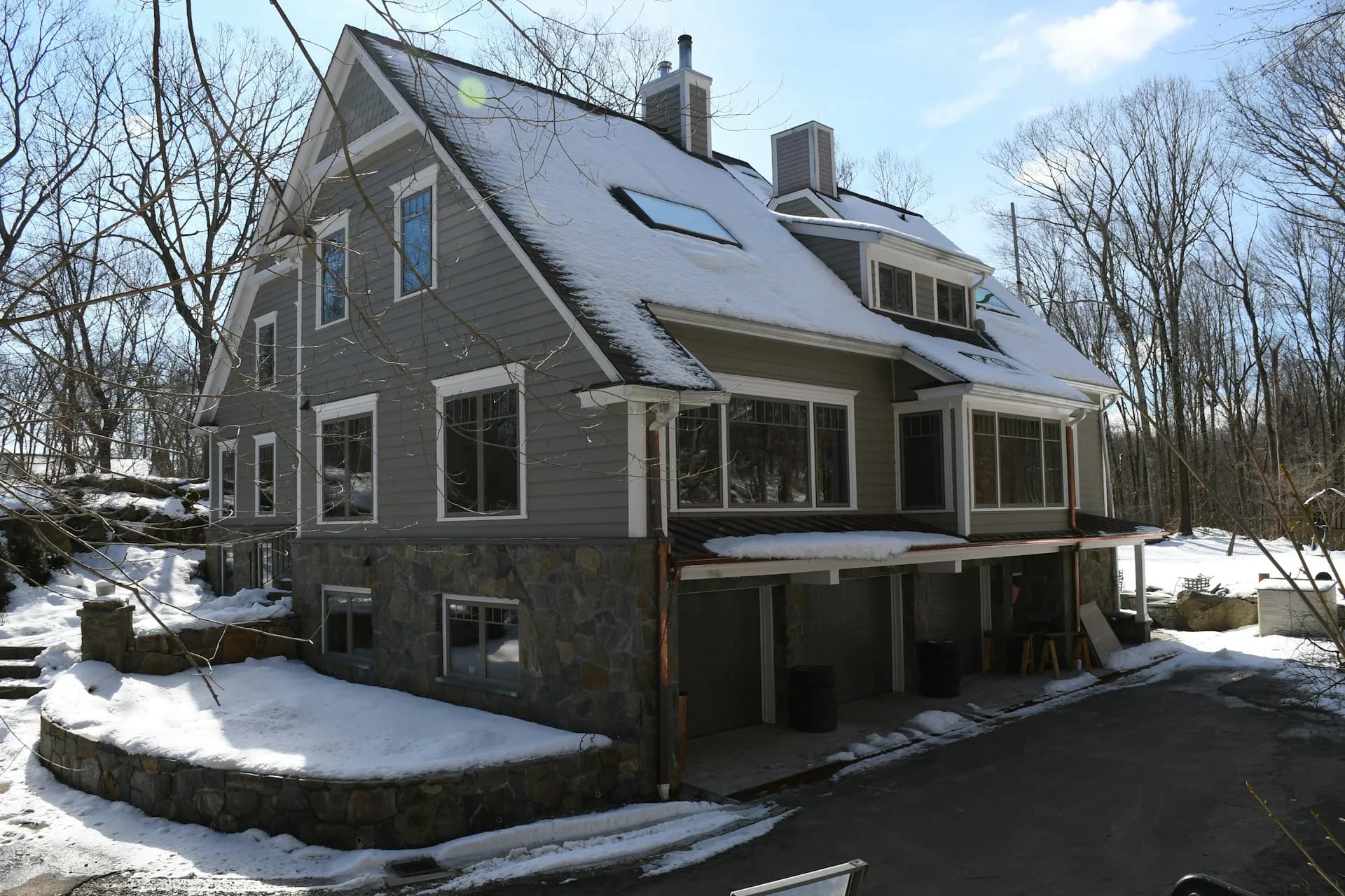 Modern residential home with dark gray siding, multiple gable roofs, and solar panels, set among bare trees with snow on the ground, designed by Talo Architect, P.C.