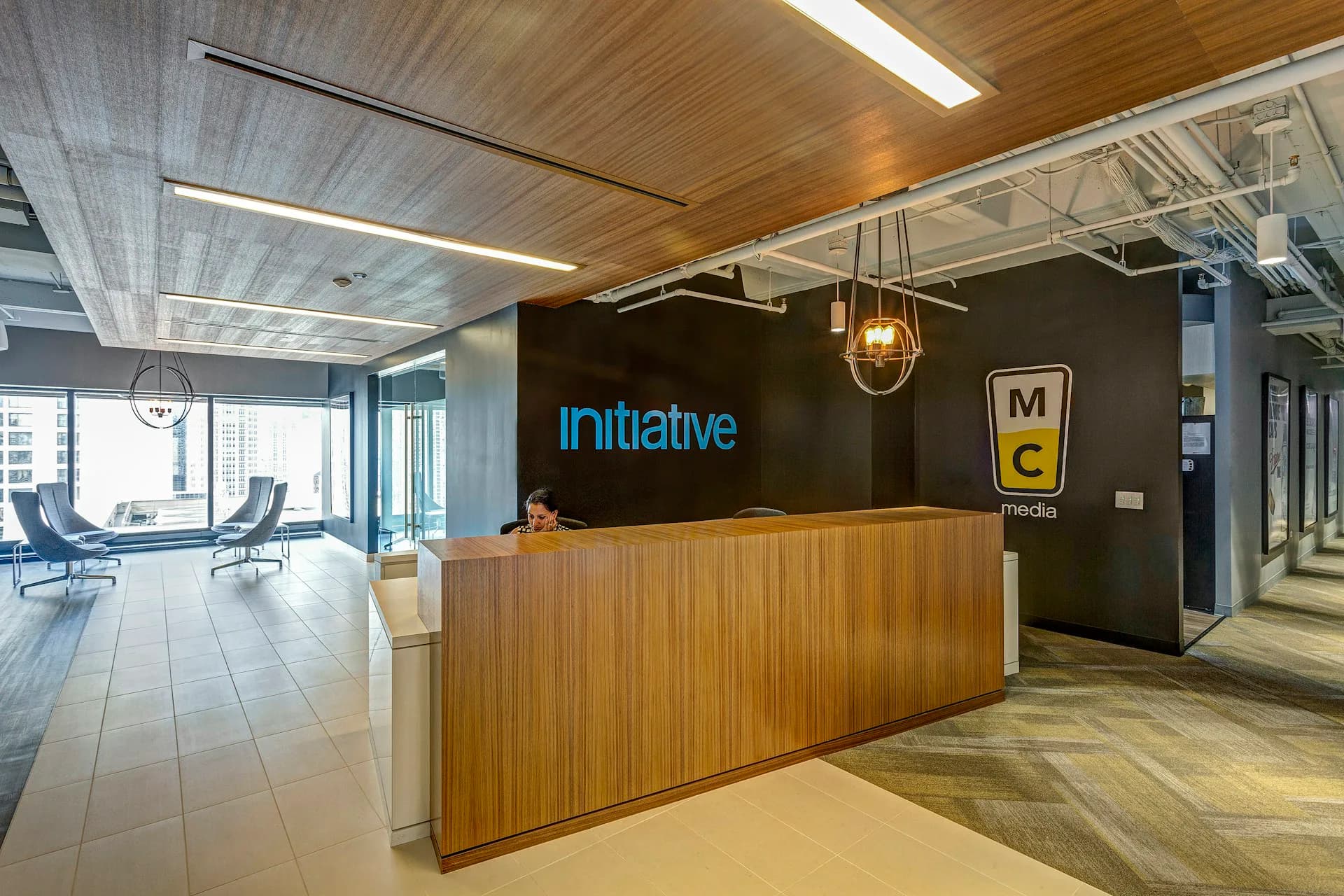 Modern office reception area with wooden slat desk, blue neon 'initiative' signage, and warm wood ceiling by Ted Moudis Associates.