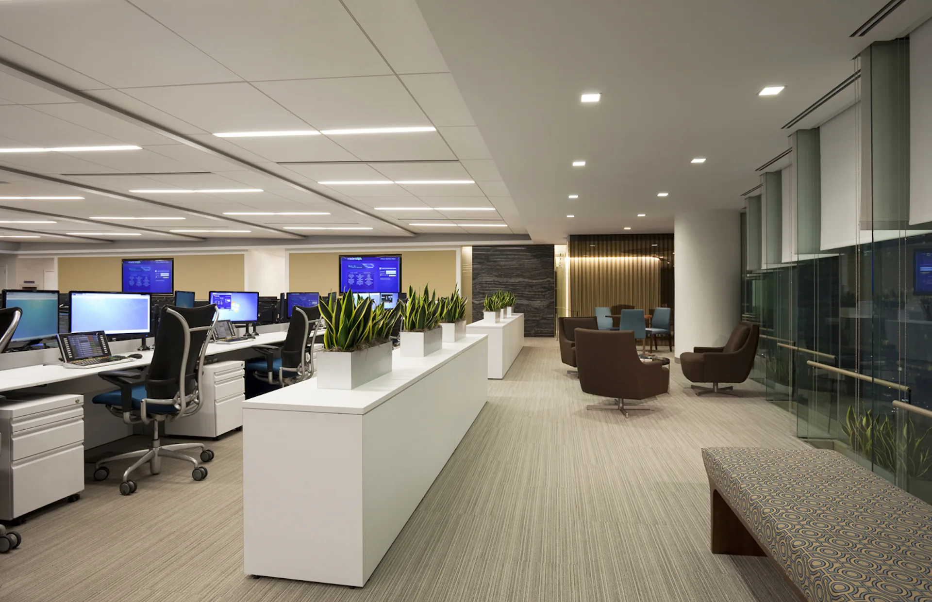 Modern office interior with white reception desk, workstations with blue screens, lounge seating, and floor-to-ceiling windows rendered by Ted Moudis Associates.