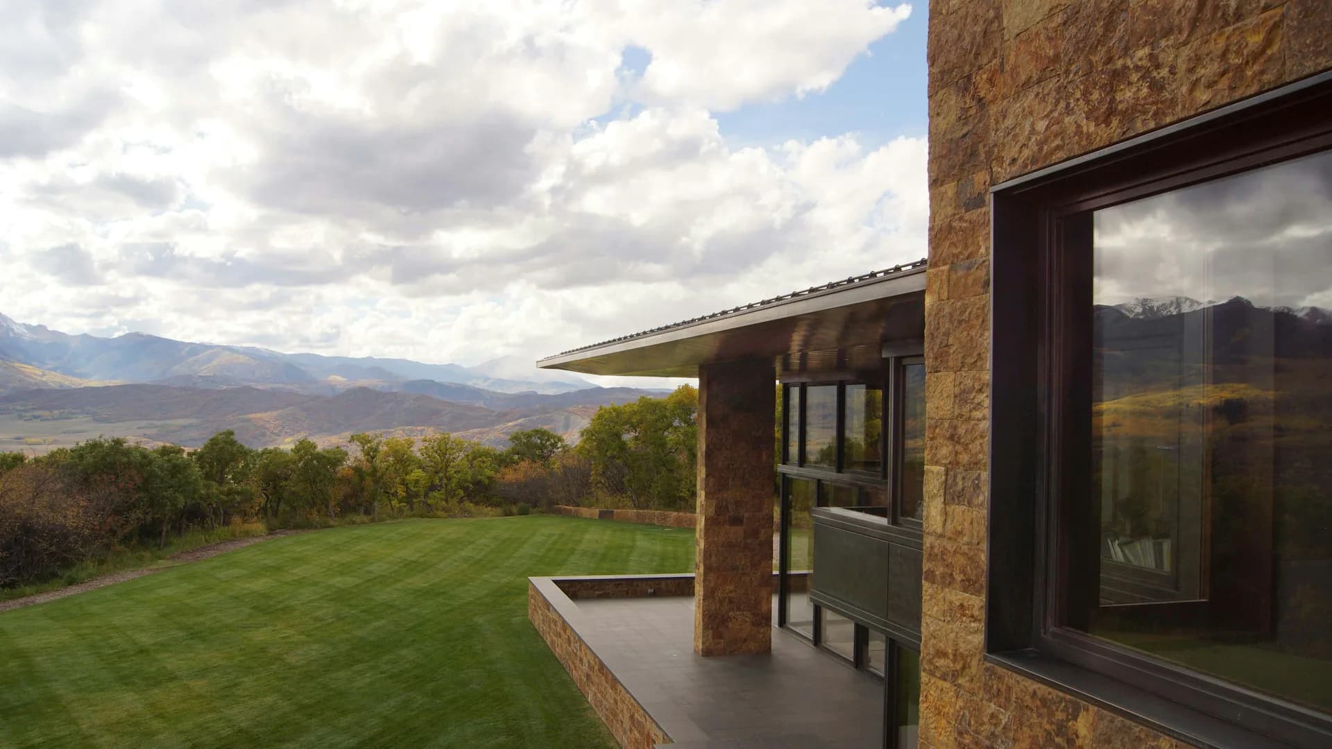 Modern brick residence with expansive windows overlooking manicured lawn and distant mountains under cloudy sky by Ted Porter Architecture.