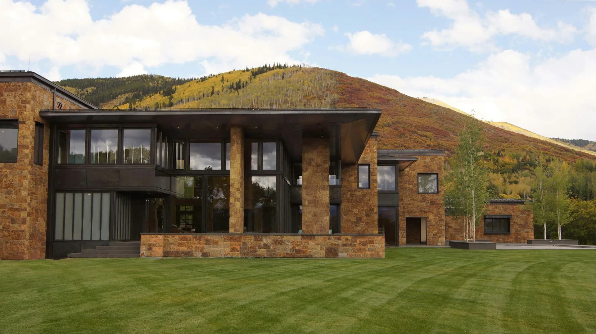 Modern brick residential building with dark metal cladding and large glazed areas set against hillside landscape with manicured lawn by Ted Porter Architecture.