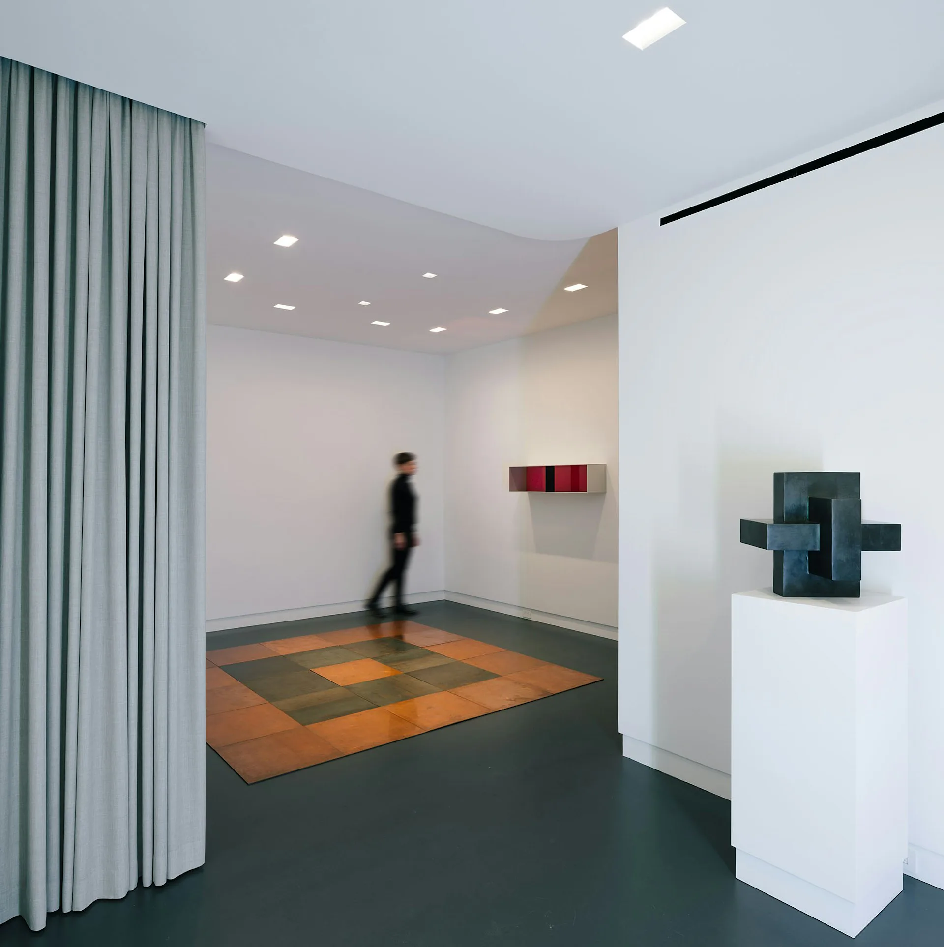 Modern gallery space with geometric floor pattern, white walls, and sculptural art installations, designed by Ted Porter Architecture.