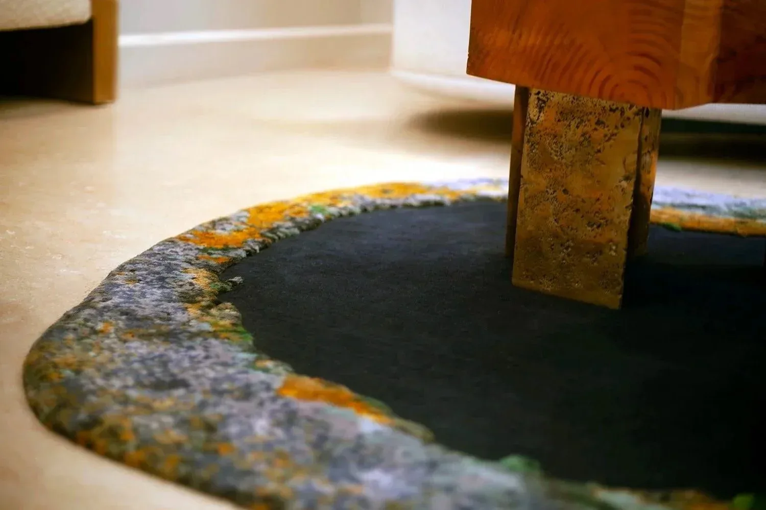 Close-up detail of a custom rug with textured border in grey, yellow, and blue tones, anchored by wooden furniture leg, by Temple Rugs.