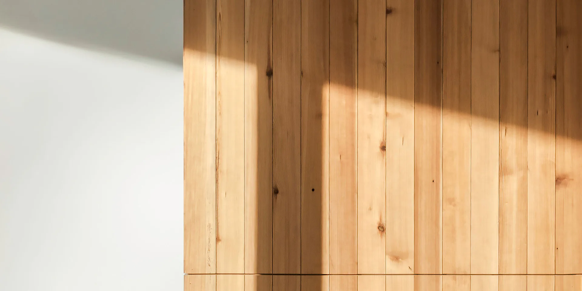 Minimalist interior with warm wooden vertical paneling and soft natural light casting geometric shadows on white wall, by TenBerke.