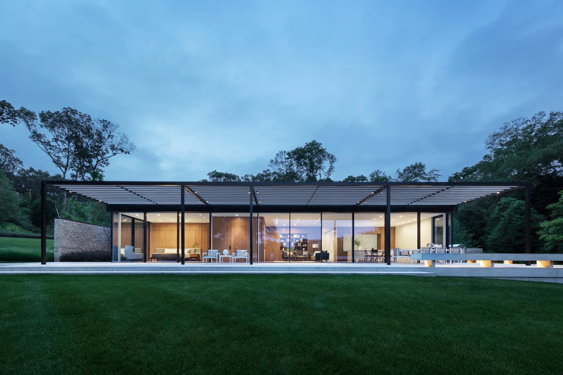 Modern single-story residential pavilion with extensive glazing, black steel framing, and minimalist design overlooking manicured lawn at dusk by TenBerke.
